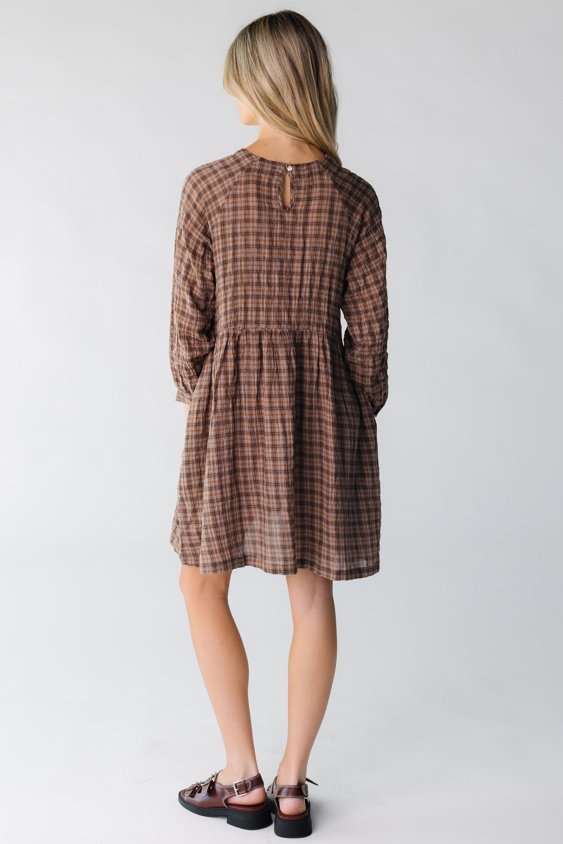 Back view of woman wearing a ight brown dress in a plaid pattern with a button and keyhole closure