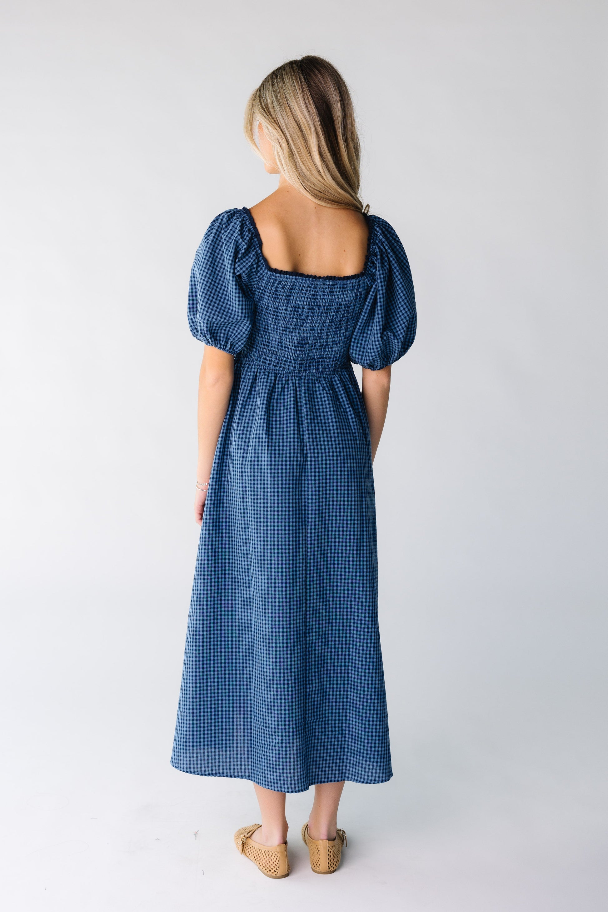 Back view of a woman wearing a blue gingham midi dress with square neckline
