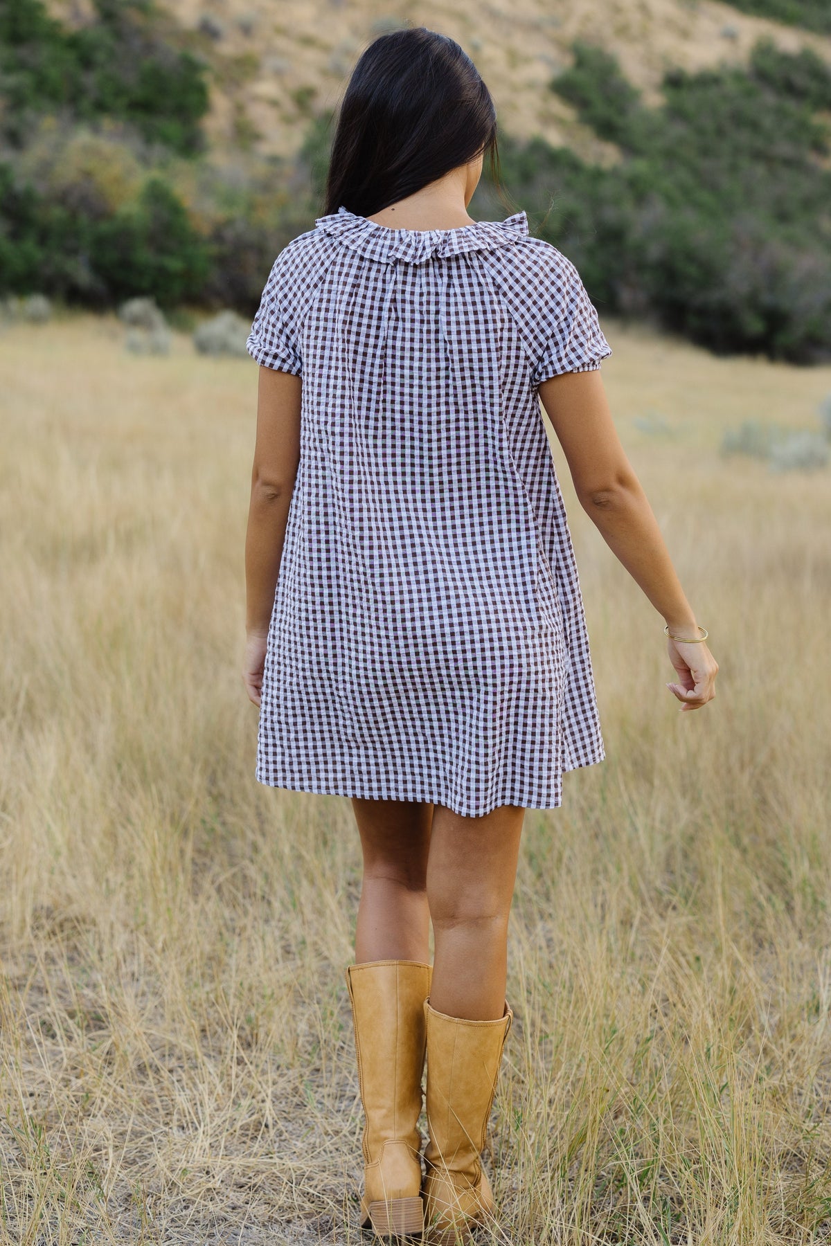 Back view of a woman wearing a brown & white gingham short dress with short puff sleeves and ruffed collar.