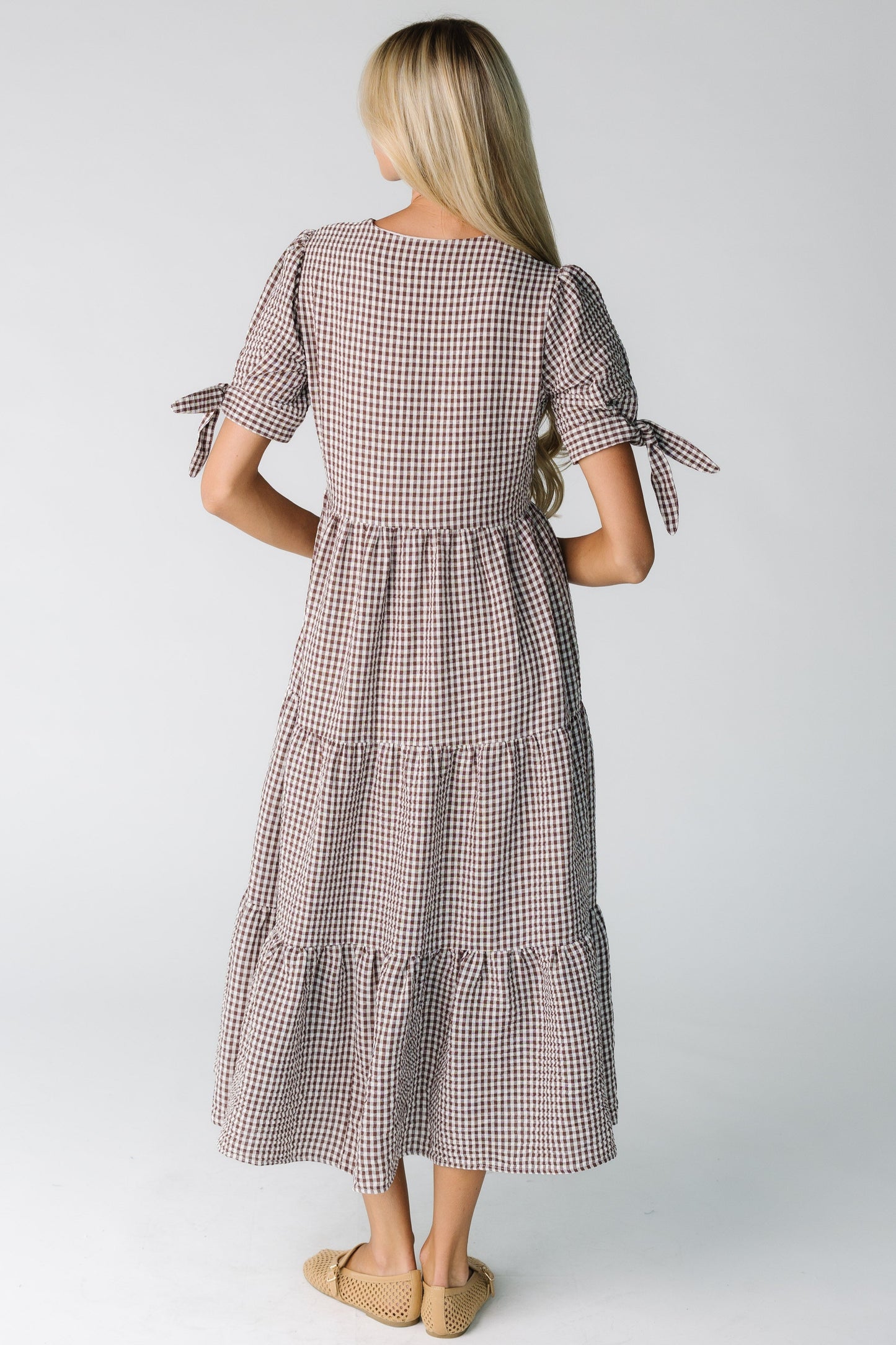 Back view of a woman wearing a brown gingham midi dress with multiple tiers