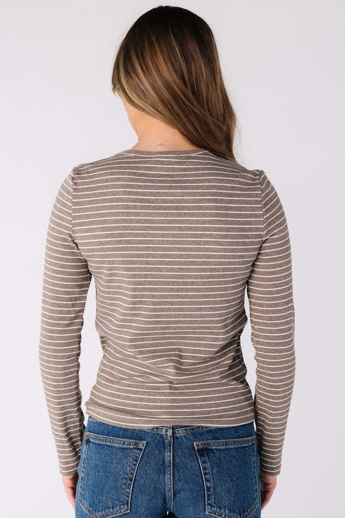 Back view of a woman wearing a beige and ivory stripe too with long sleeves