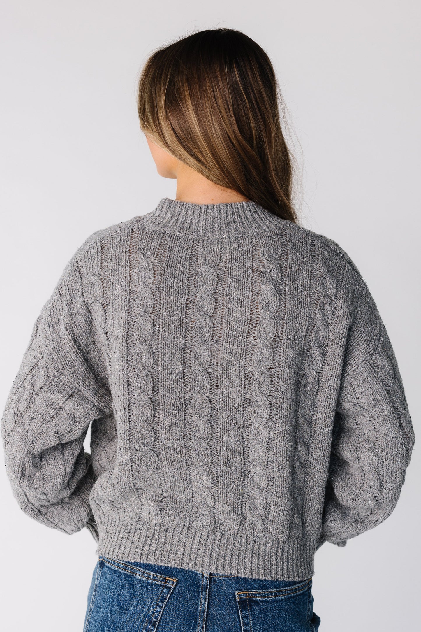 Back view of a woman wearing a grey cable knit sweater
