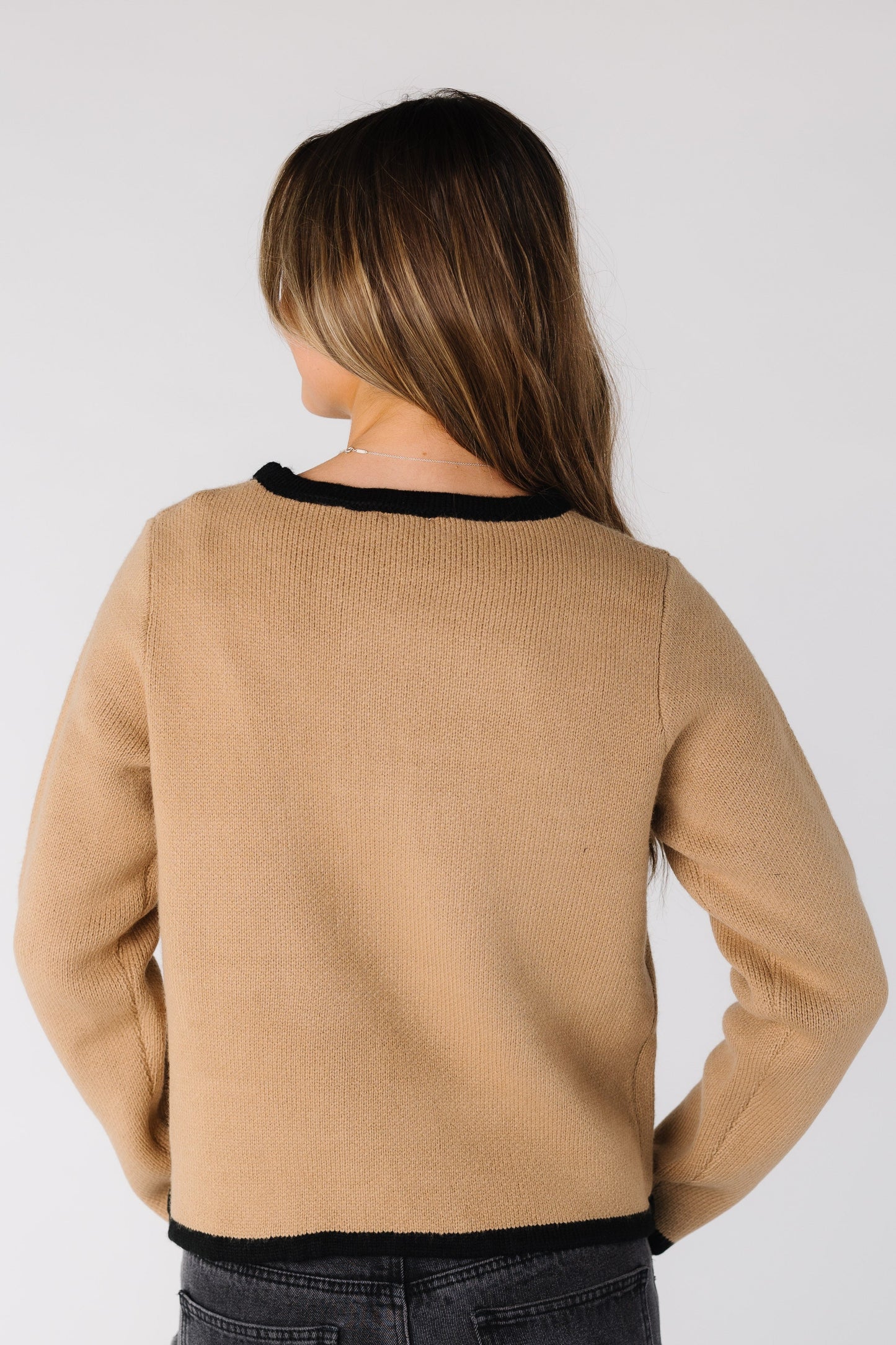 Back view of a woman wearing a camel cardigan with black trim