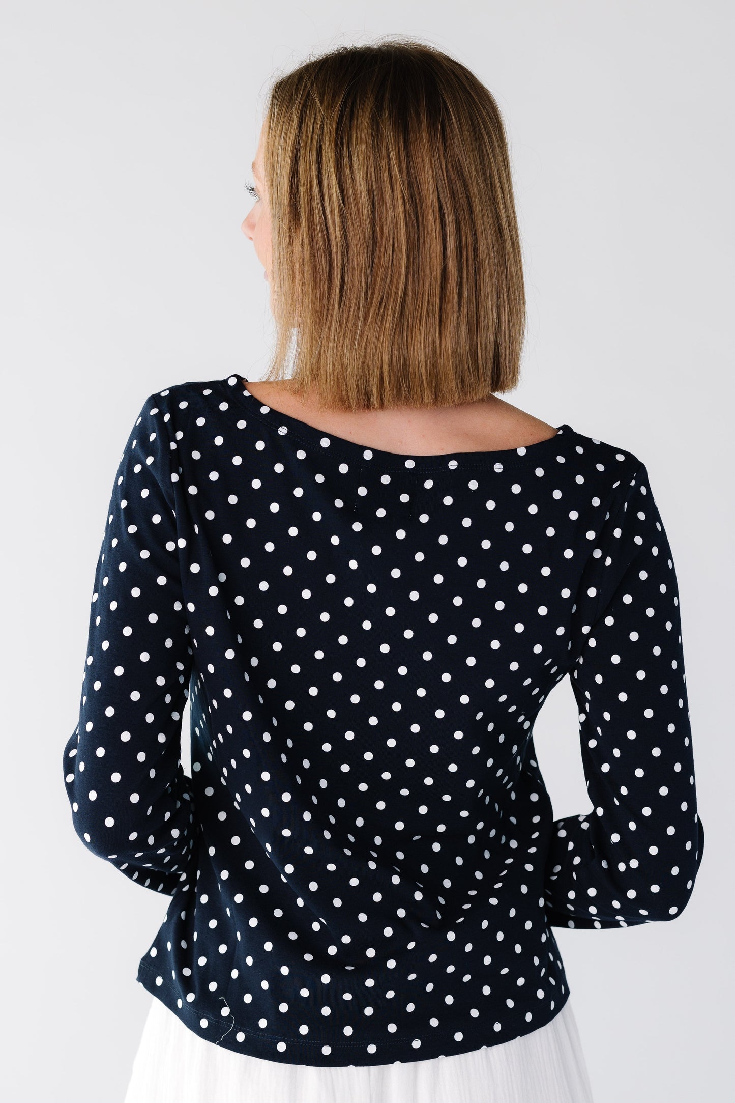 Back view of a woman wearing a navy polka dot top with wider neckline