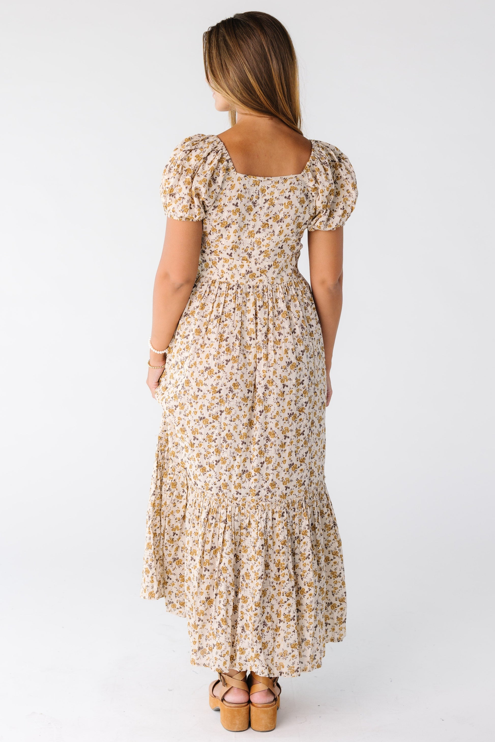 Back view of a woman wearing a gold floral midi maxi dress with a square neckline