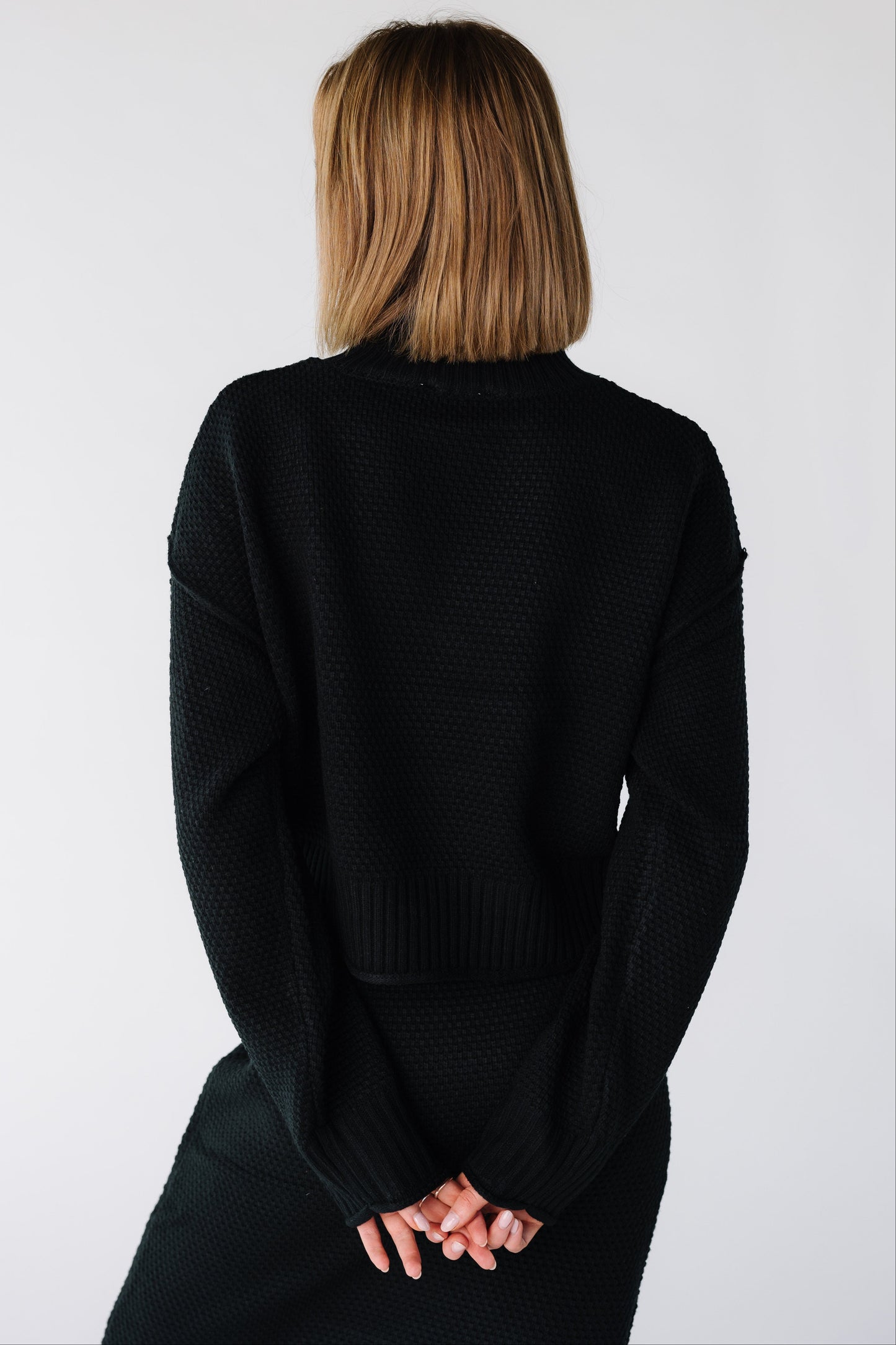 Back view of a woman wearing a black long sleeve sweater and skirt set