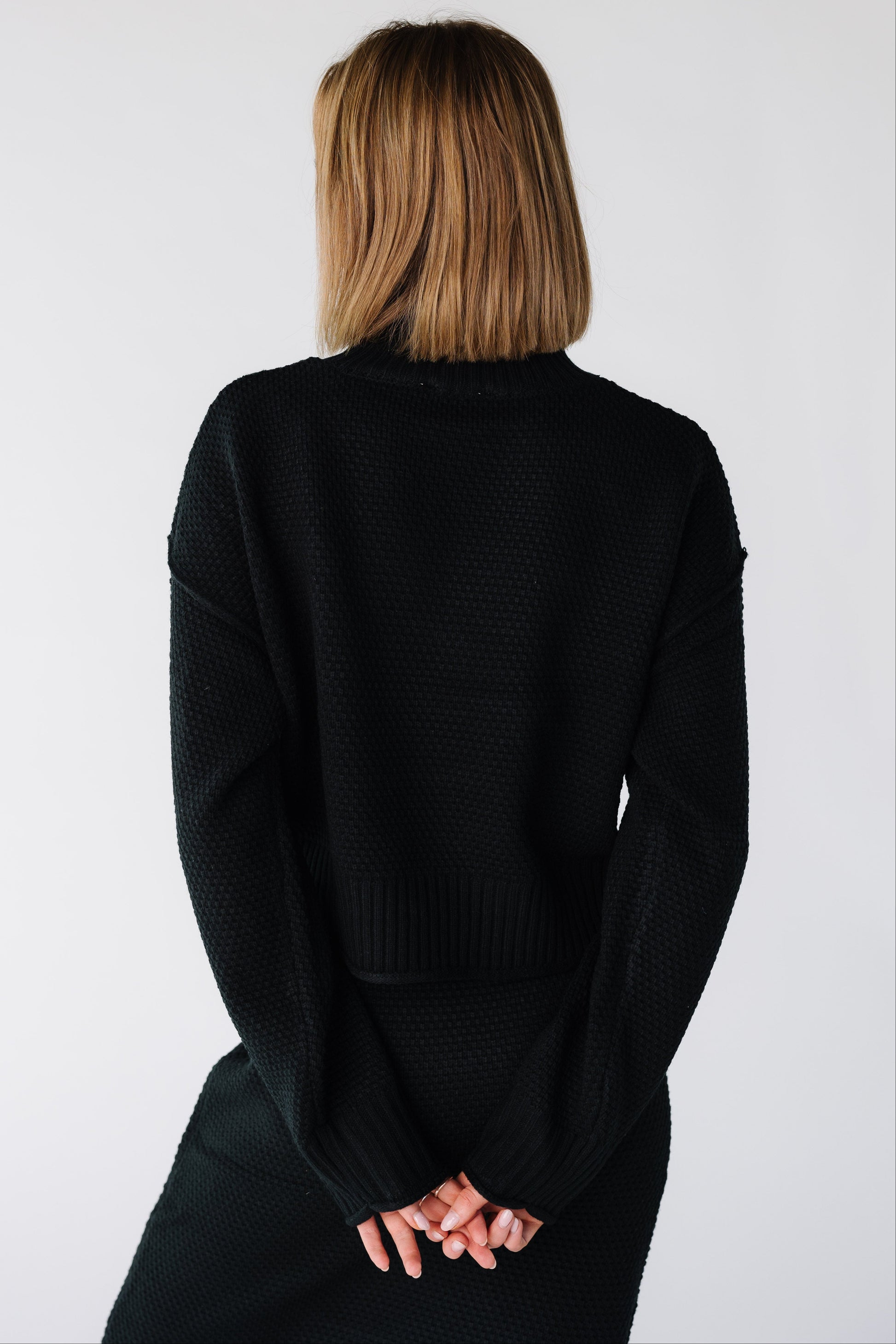 Back view of a woman wearing a black long sleeve sweater and skirt set