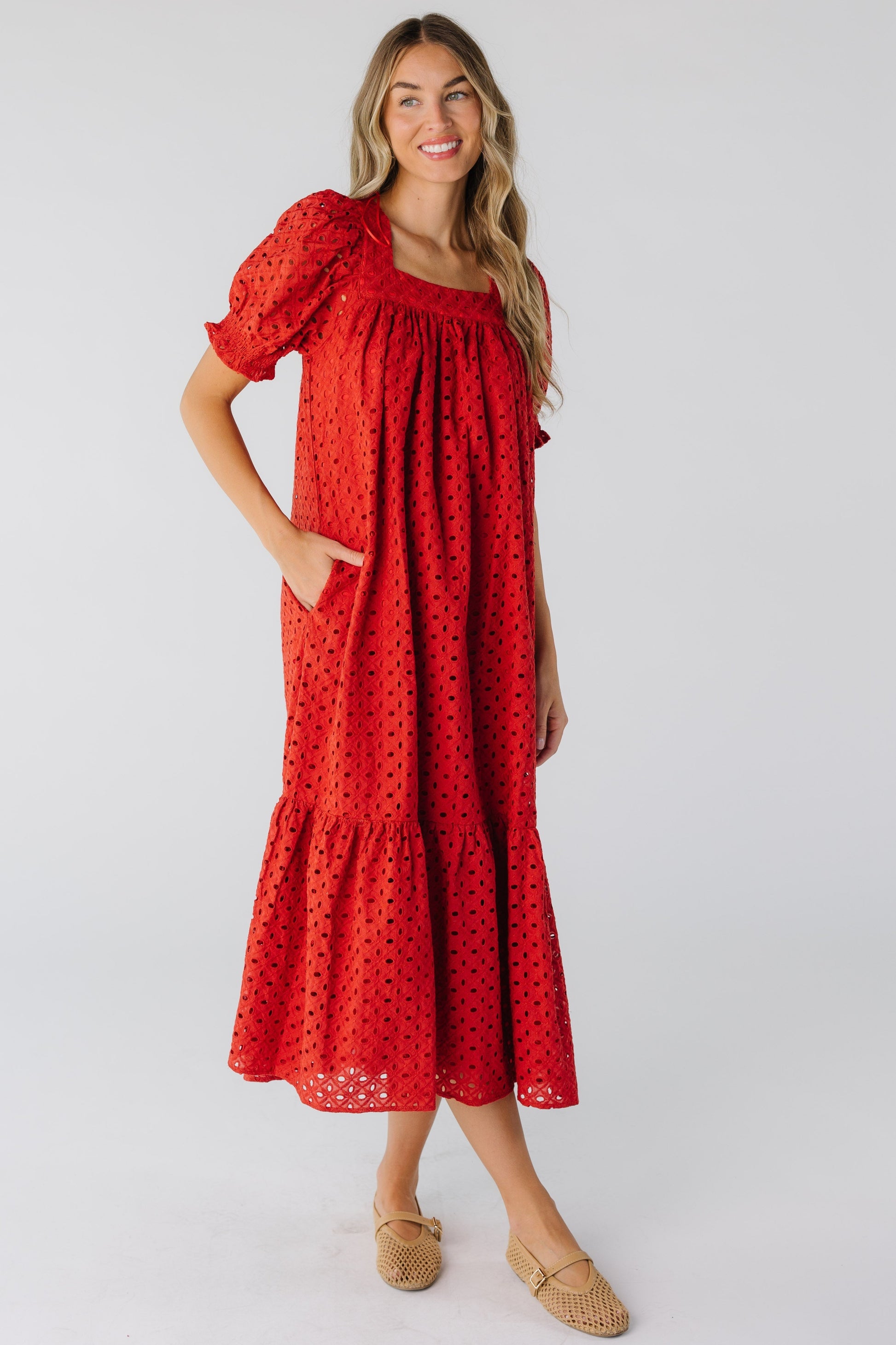 A woman wearing a red eyelet midi dress with short puff sleeves and square neckline.