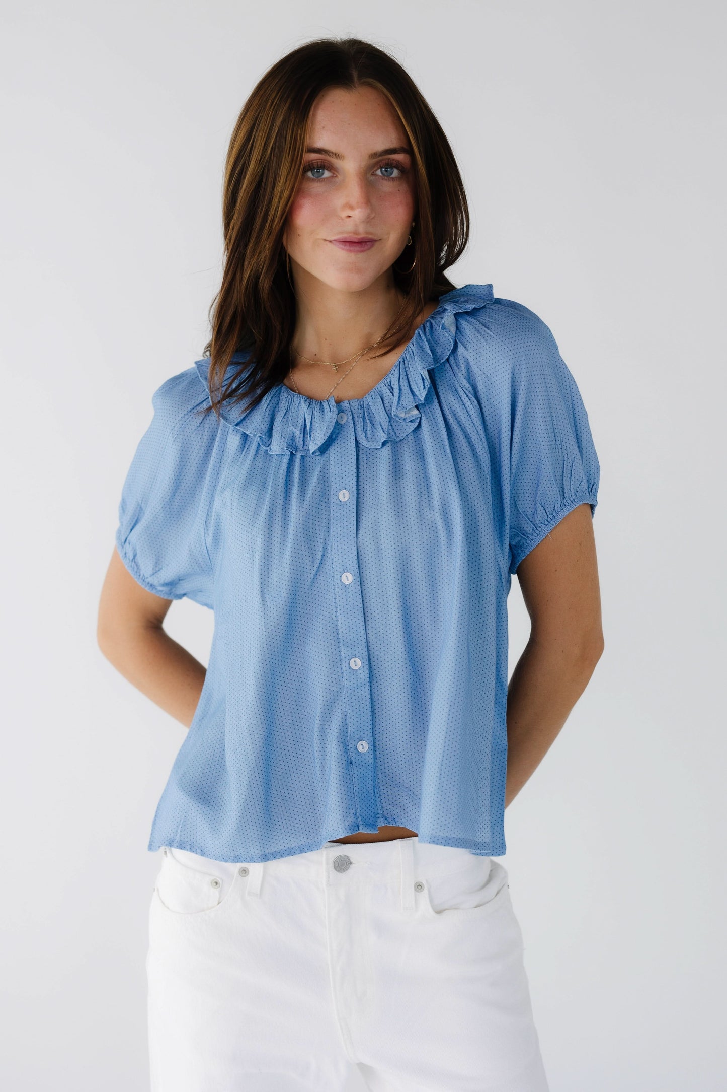 Young woman wearing a blue polka dot button down blouse with short puff sleeves and a round ruffled collar.