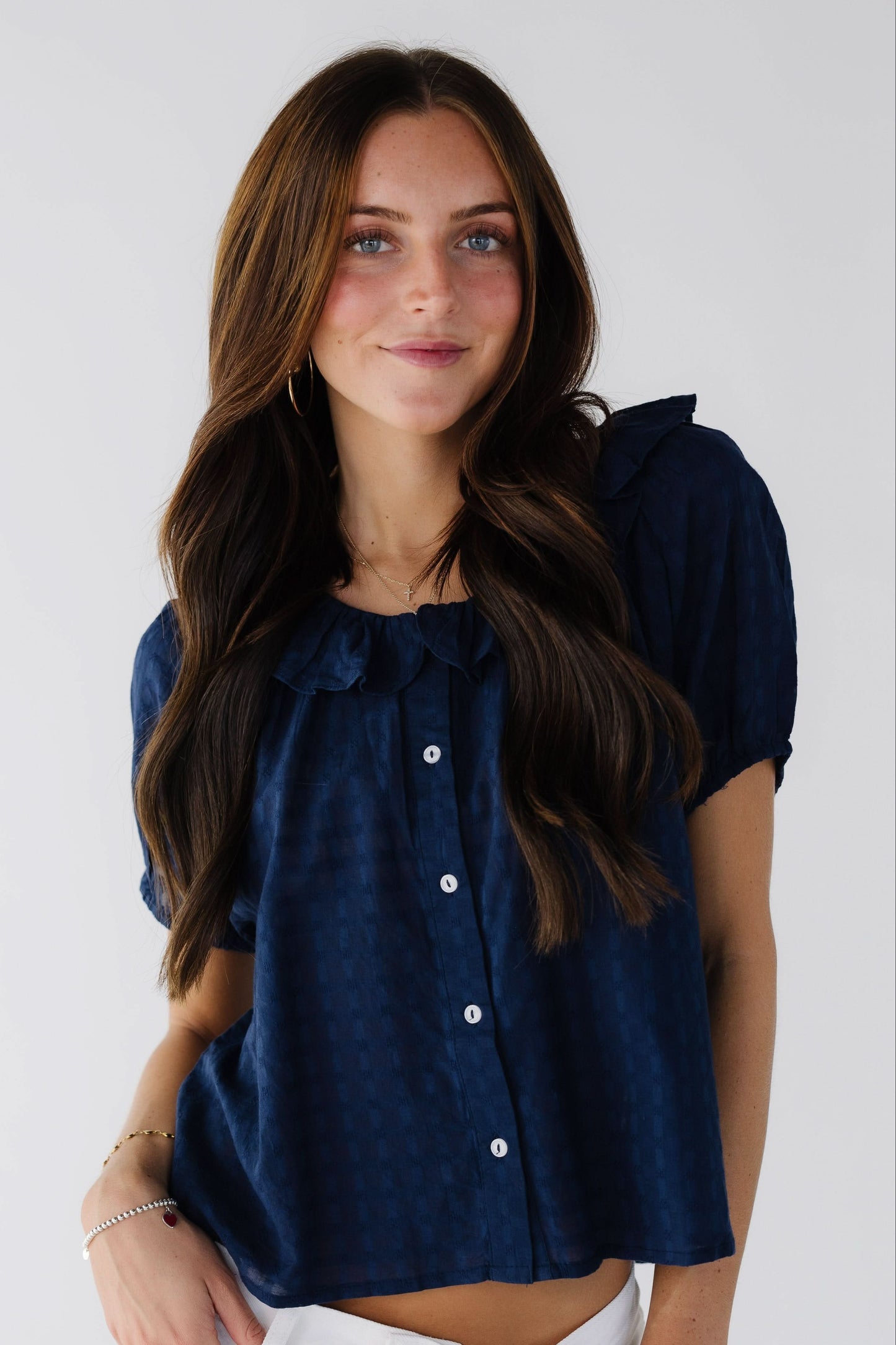 Young woman wearing a modest navy button down blouse with a ruffle collar and short sleeves.