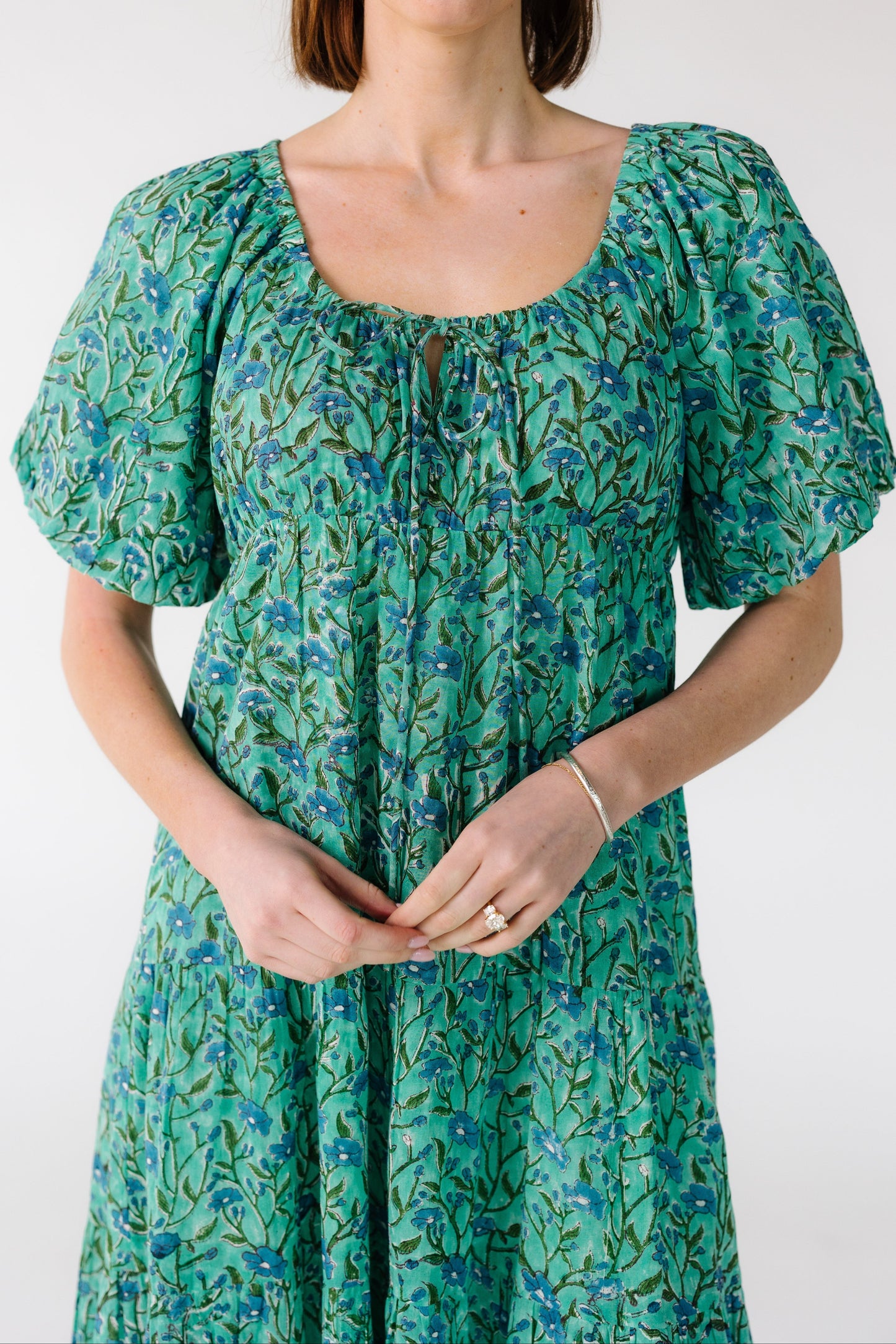Close view of a woman wearing a teal floral print dress with a drawstring scoop neckline and balloon sleeves.