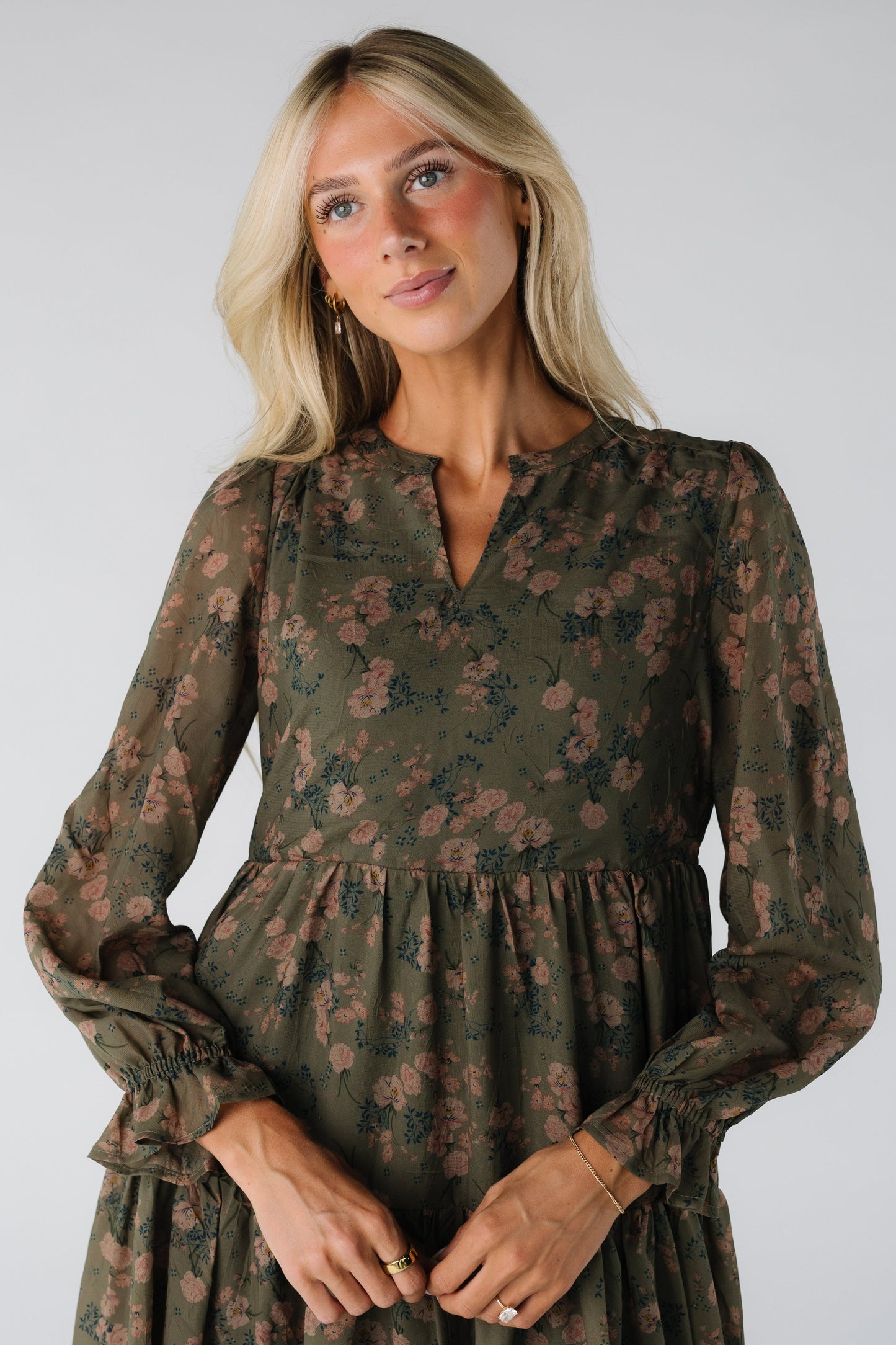 Close view of a woman wearing an olive floral print dress with V-neckline and long sleeves