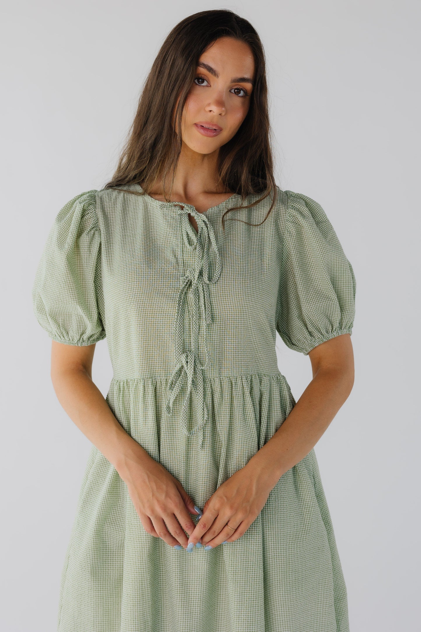 Close view of green gingham dress with round neckline, 3 tie closure and short puff sleeves