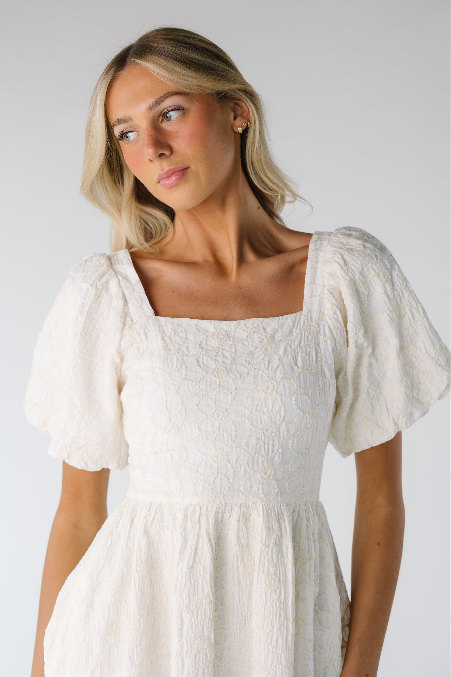 Close up view of cream embroidered dress with full short sleeves and square neckine