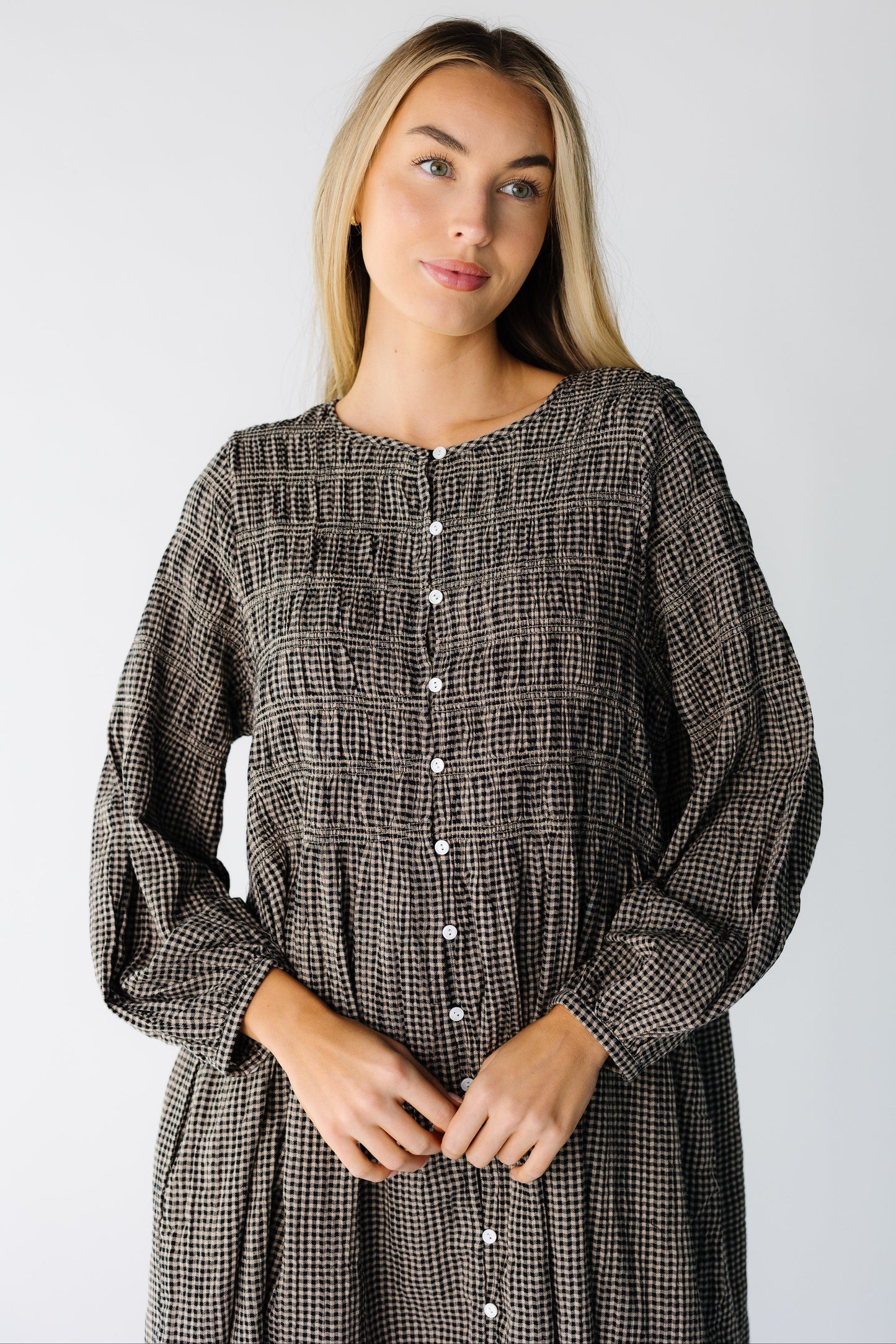 Close view of a woman wearing a black gingham button down dress with a round neckline and long sleeves