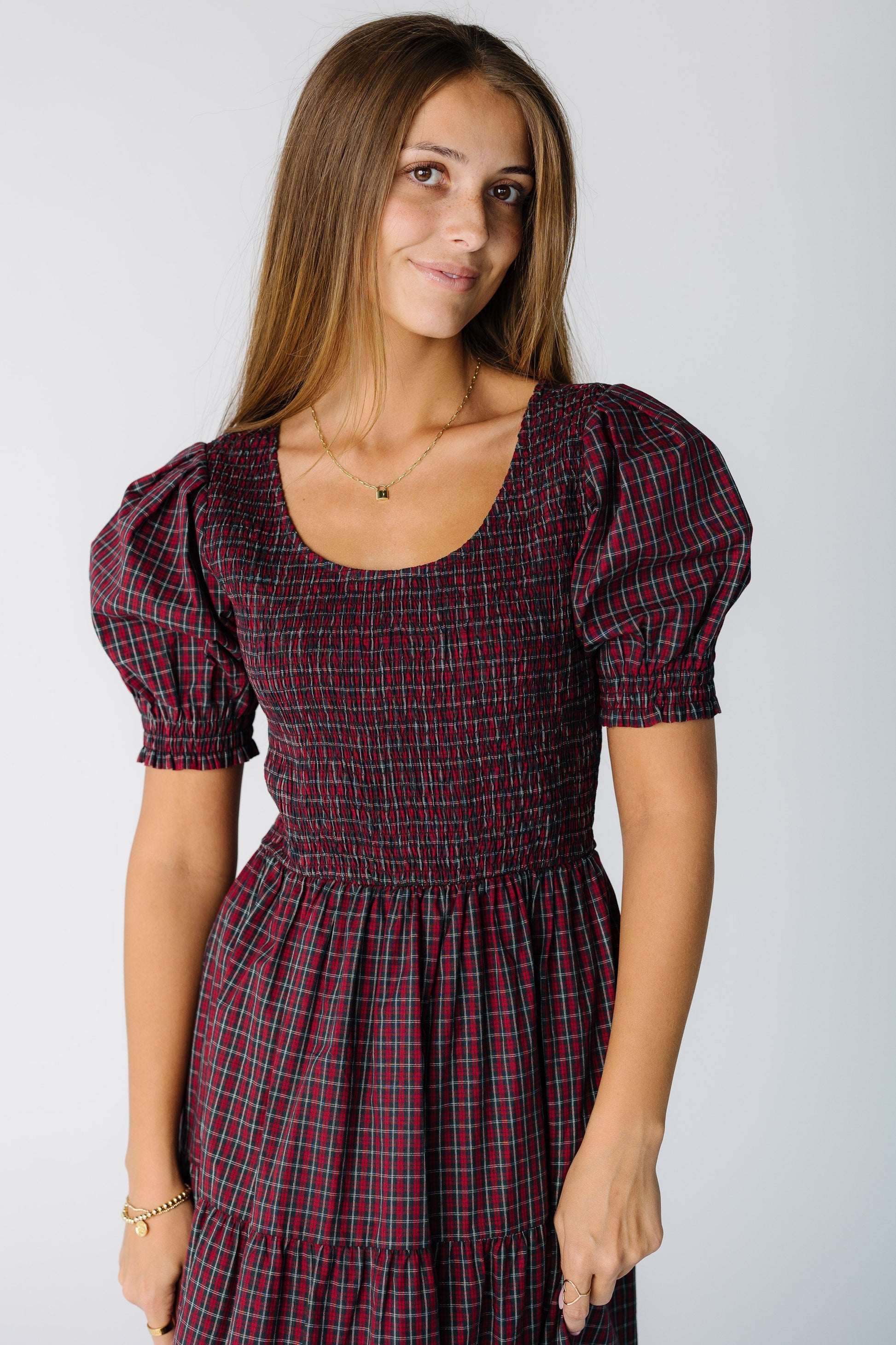 Close view of a woman wearing a red plaid dress with short sleeves, a scoop neckline and smocked bodice