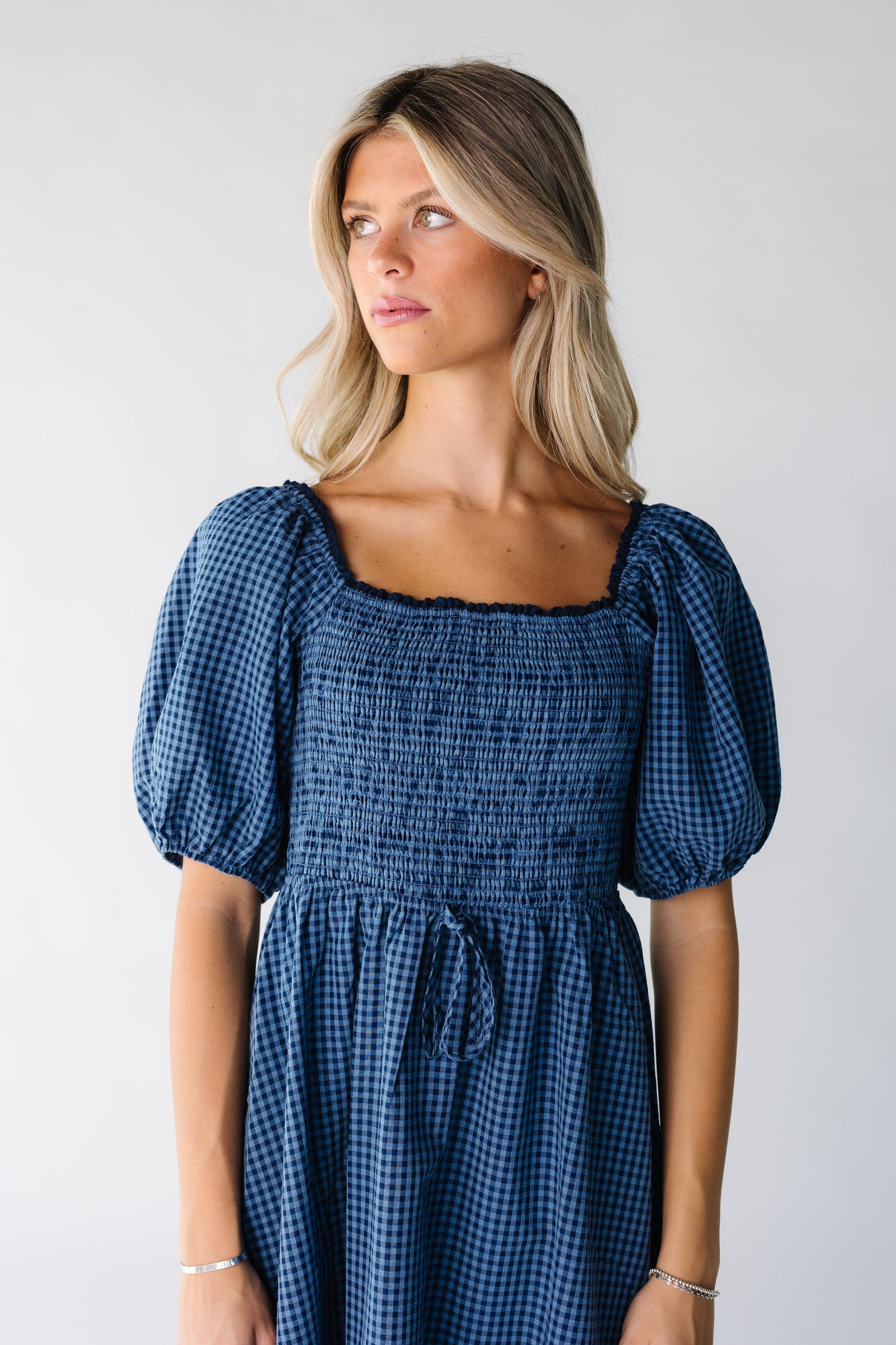 Close view of a woman wearing a blue gingham midi dress with square neckline and short puff sleeves