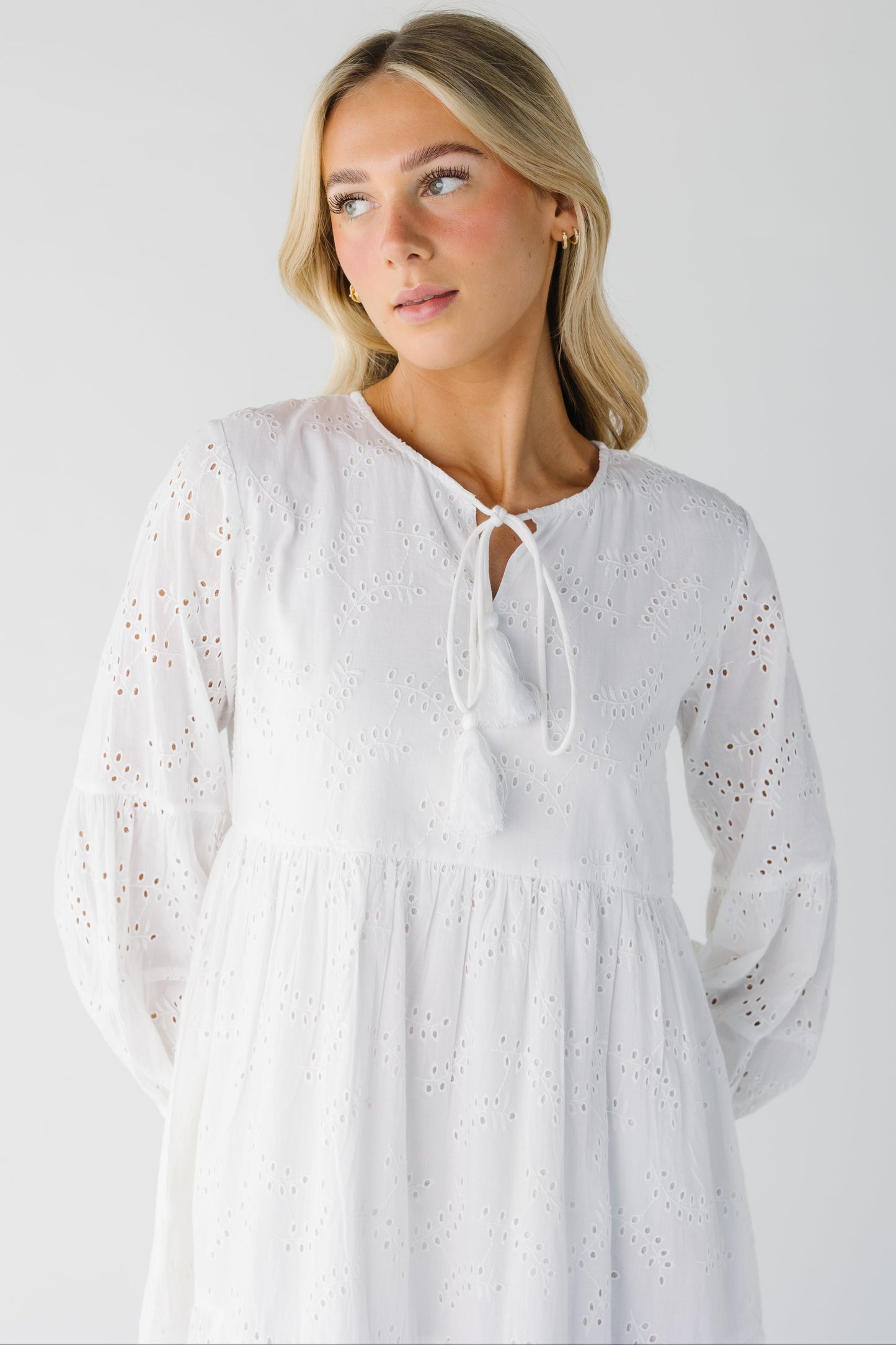 Close view of white eyelet dress with long sleeves and tie at neckline