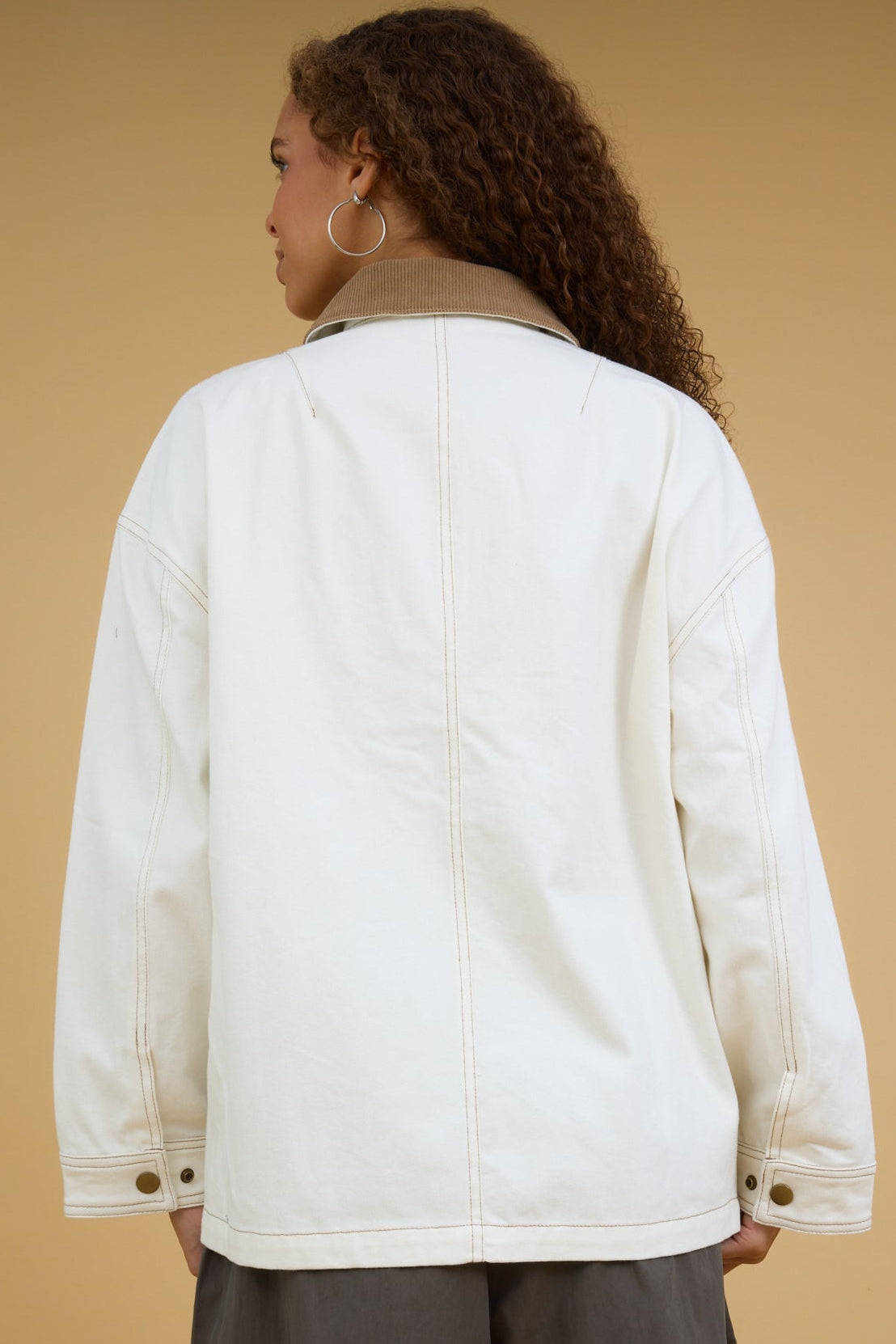 Back view of a woman wearing an ecru jacket with snap closures, contrasting stitching and a corduroy collar.