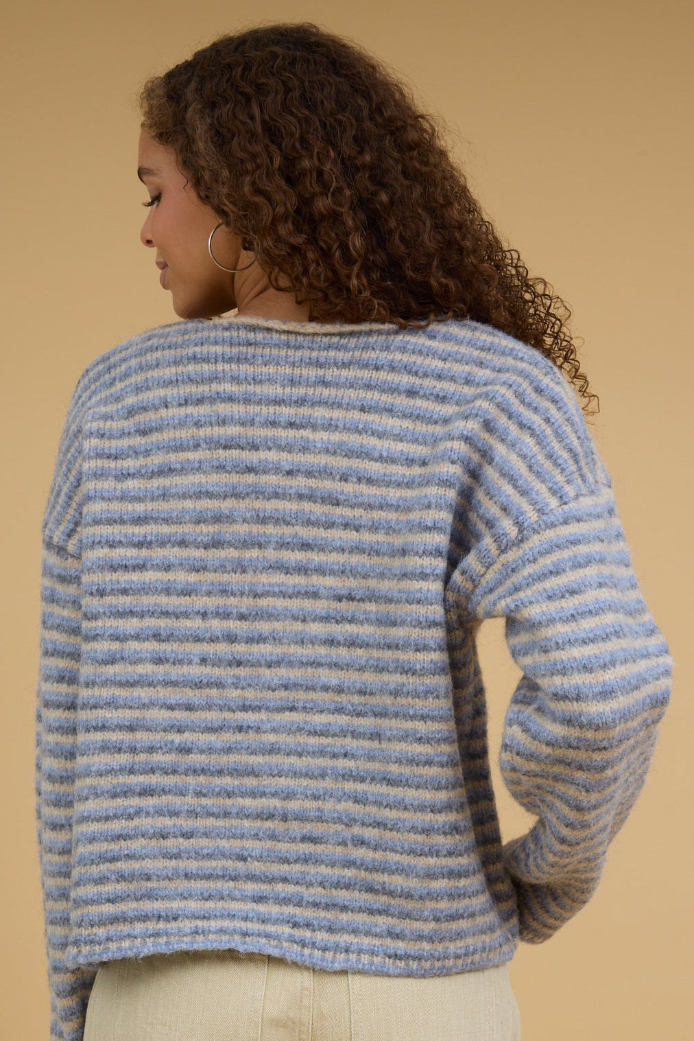 Back view of a teen girl wearing a blue-grey & taupe stripe pullover sweater with long sleeves.
