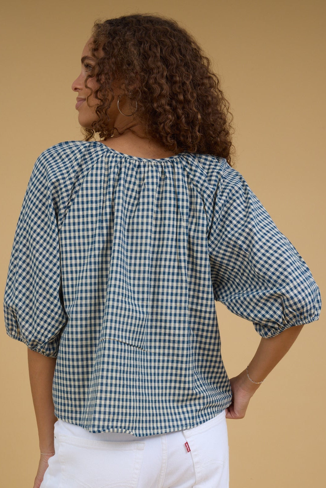 Back view of a young woman wearing a blue & cream gingham blouse.