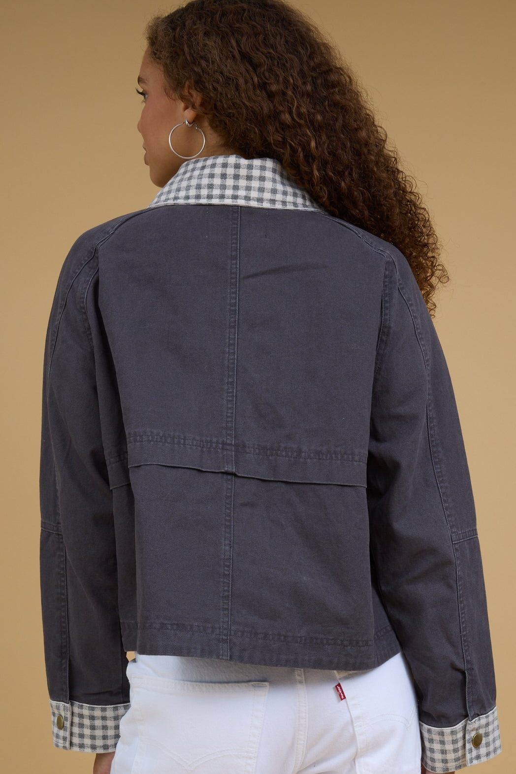 Back view of a woman wearing a charcoal jacket with gingham cuffs and gingahm collar.