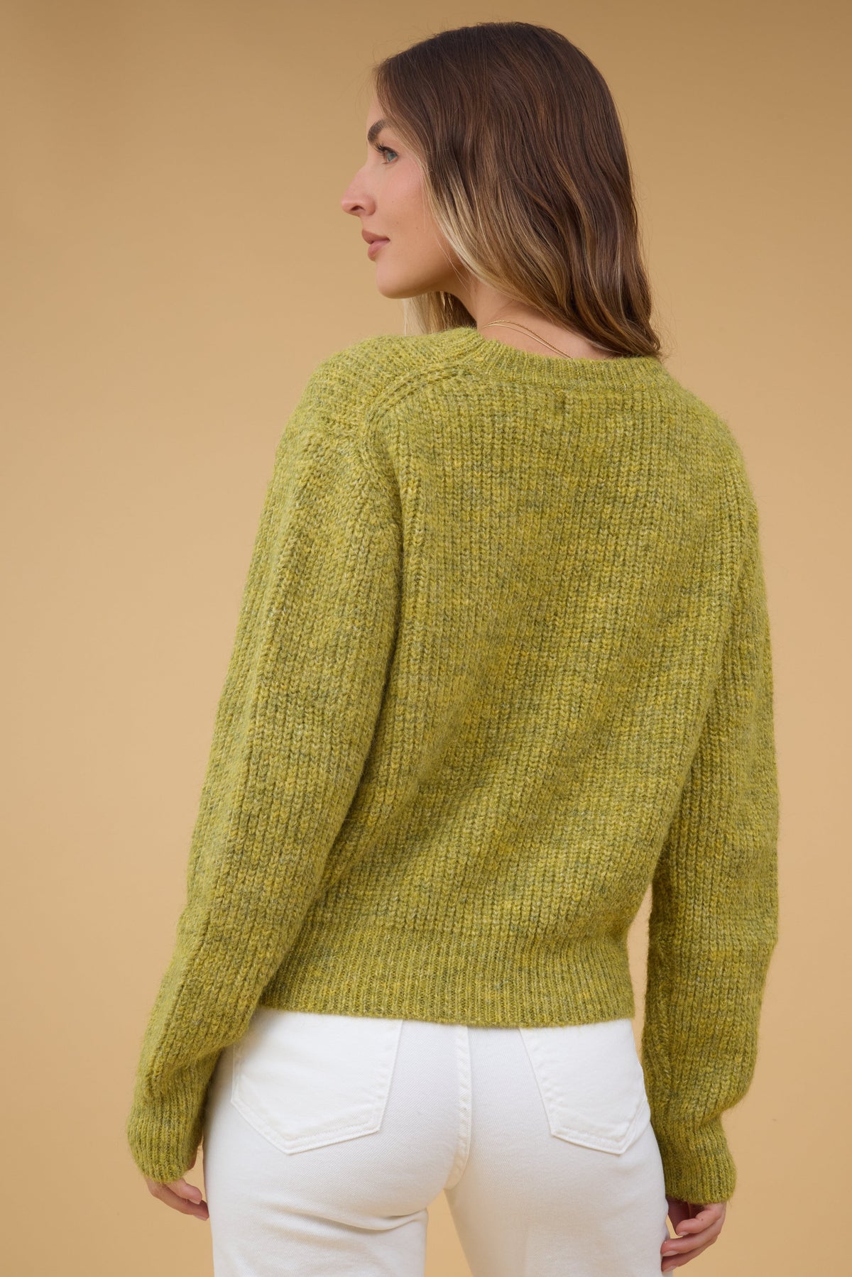 Back view of a young woman wearing an olive rib knit sweater with long sleeves.
