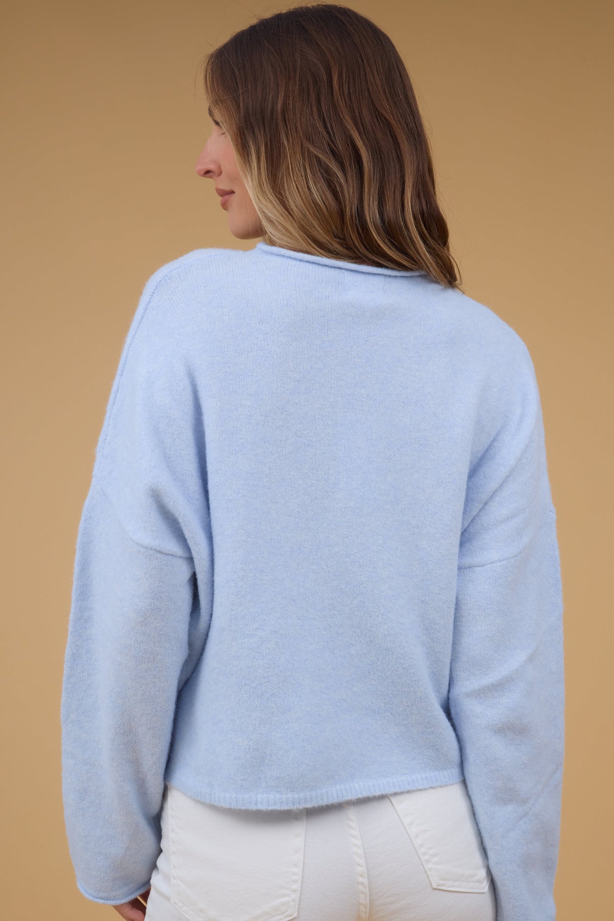 Back view of a young woman wearing a light blue sweater with drop shoulders and long sleeves.