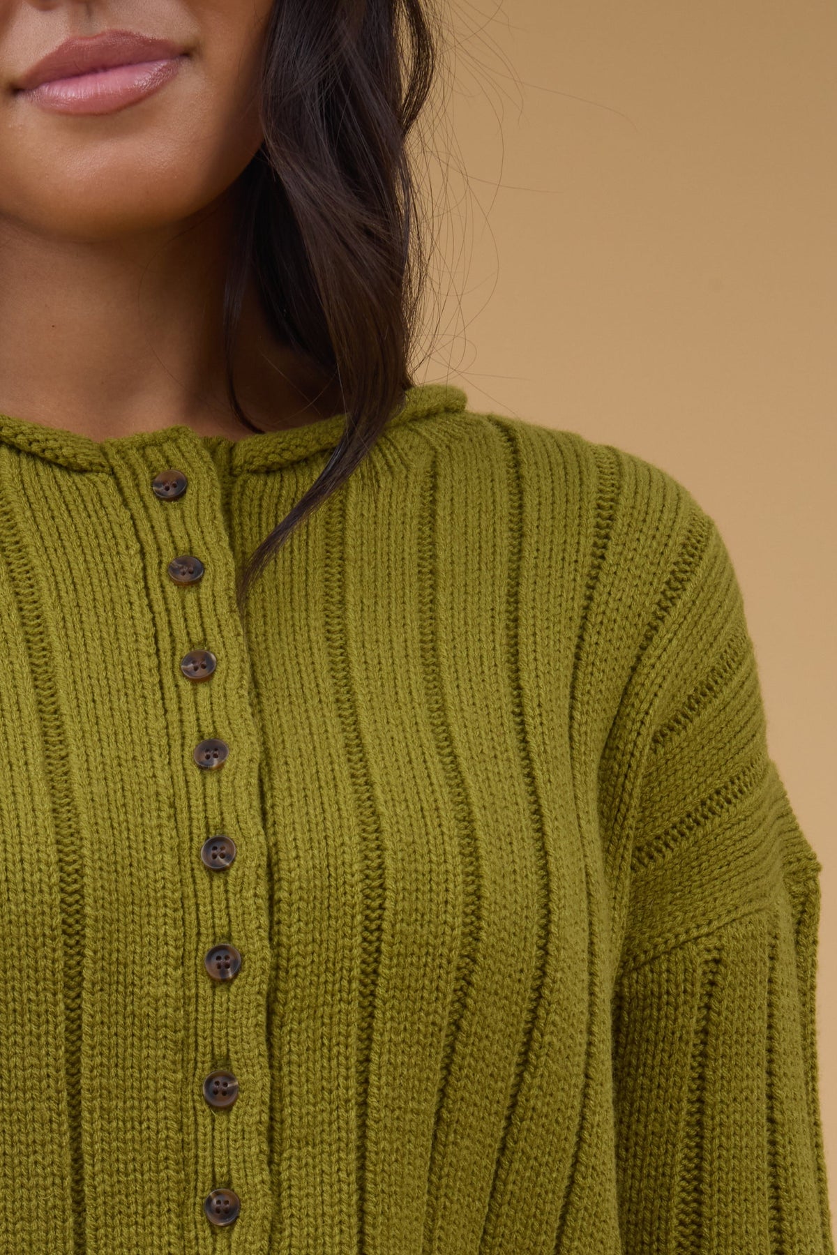 Close view of a woman wearing a wide ribbed, button down cardiganwith a rolled neckline.