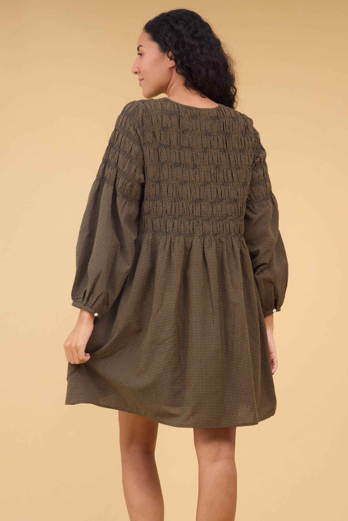 Back view of a woman wearing a loose fitting brown & black gingham dress with spaced out rows os smocking.