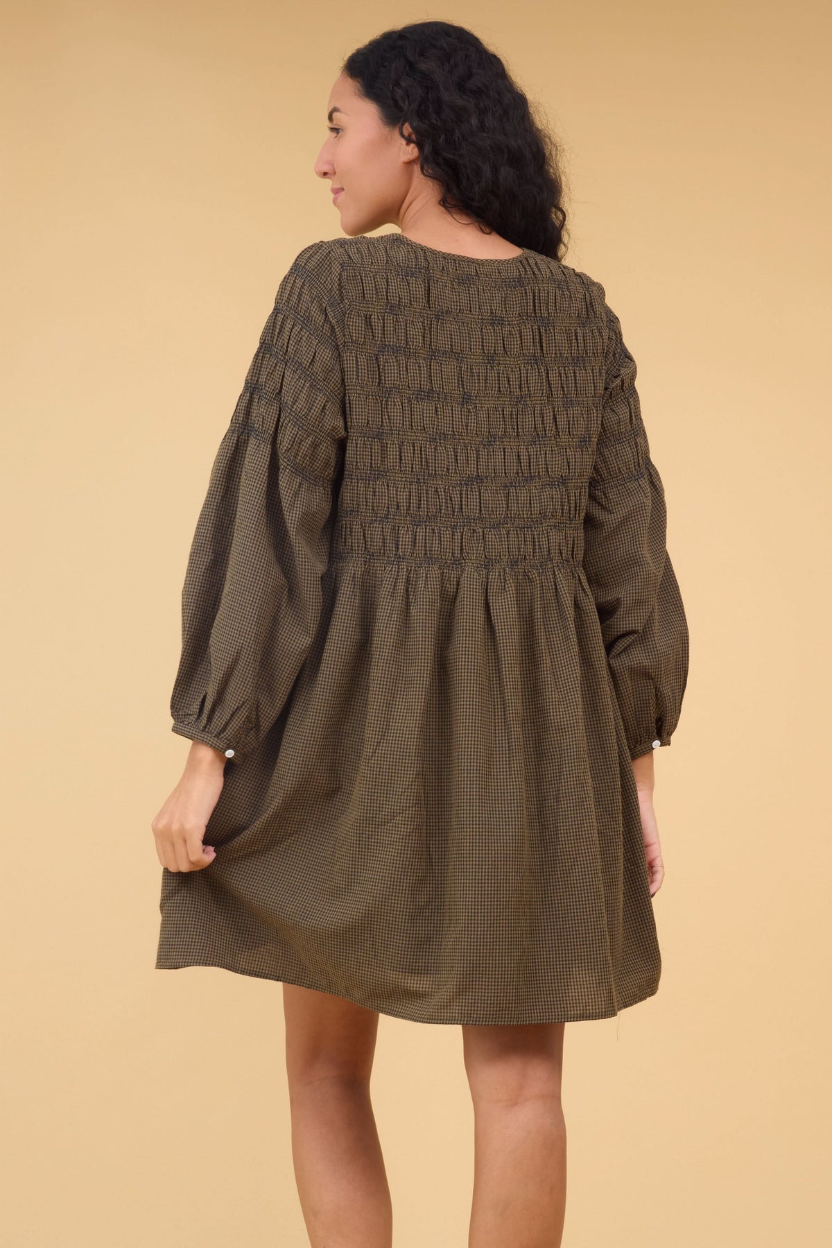 Back view of a woman wearing a loose fitting brown & black gingham dress with spaced out rows os smocking.