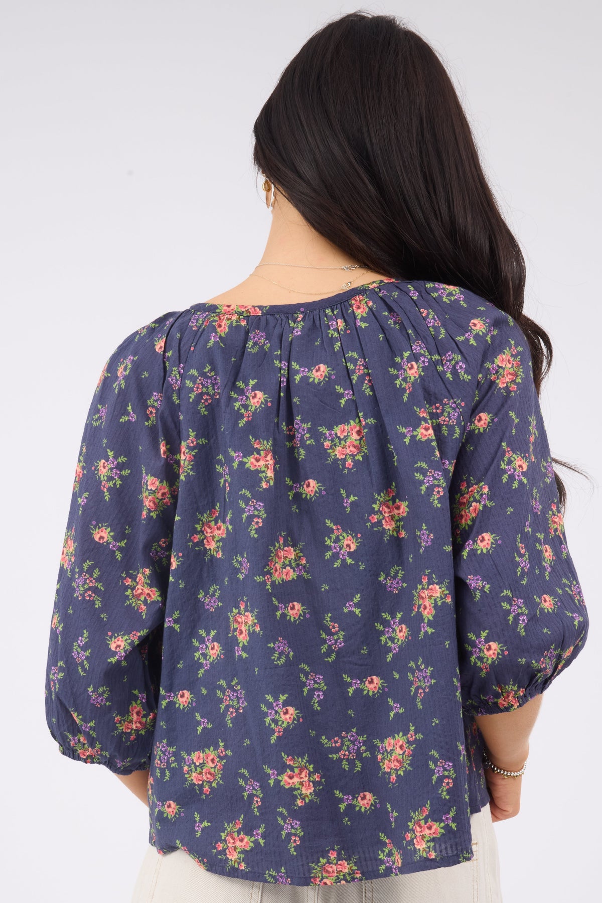 Back view of a woman wearing a blue floral flowy blouse with elbow length sleeves.