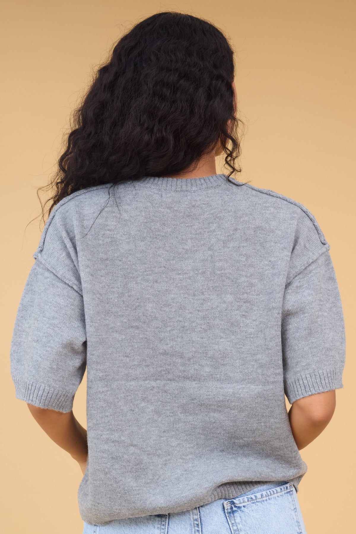 Back view of a woman wearing a grey loose fitting sweater with short sleeves and exposed seams.