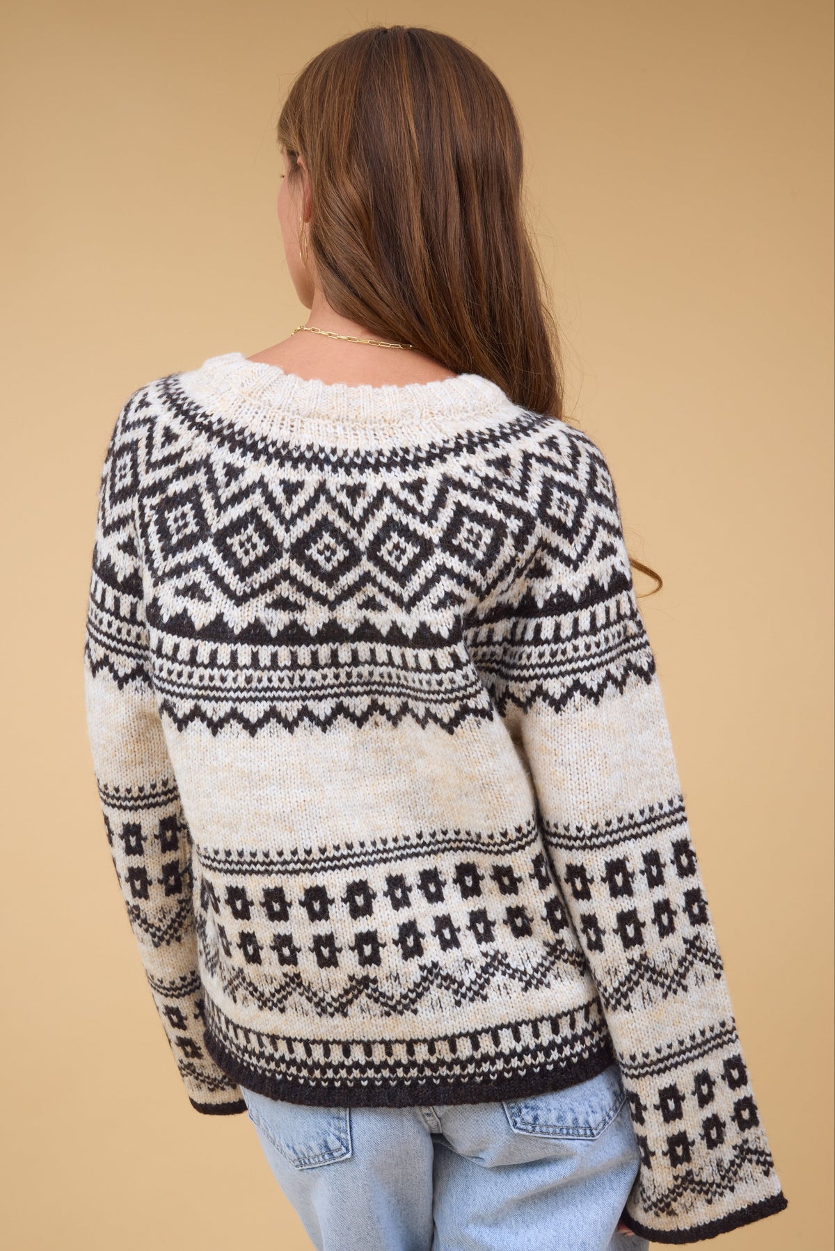 A back view of ayoung woman wearing an oatmeal & black nordic sweater with long loose sleeves.