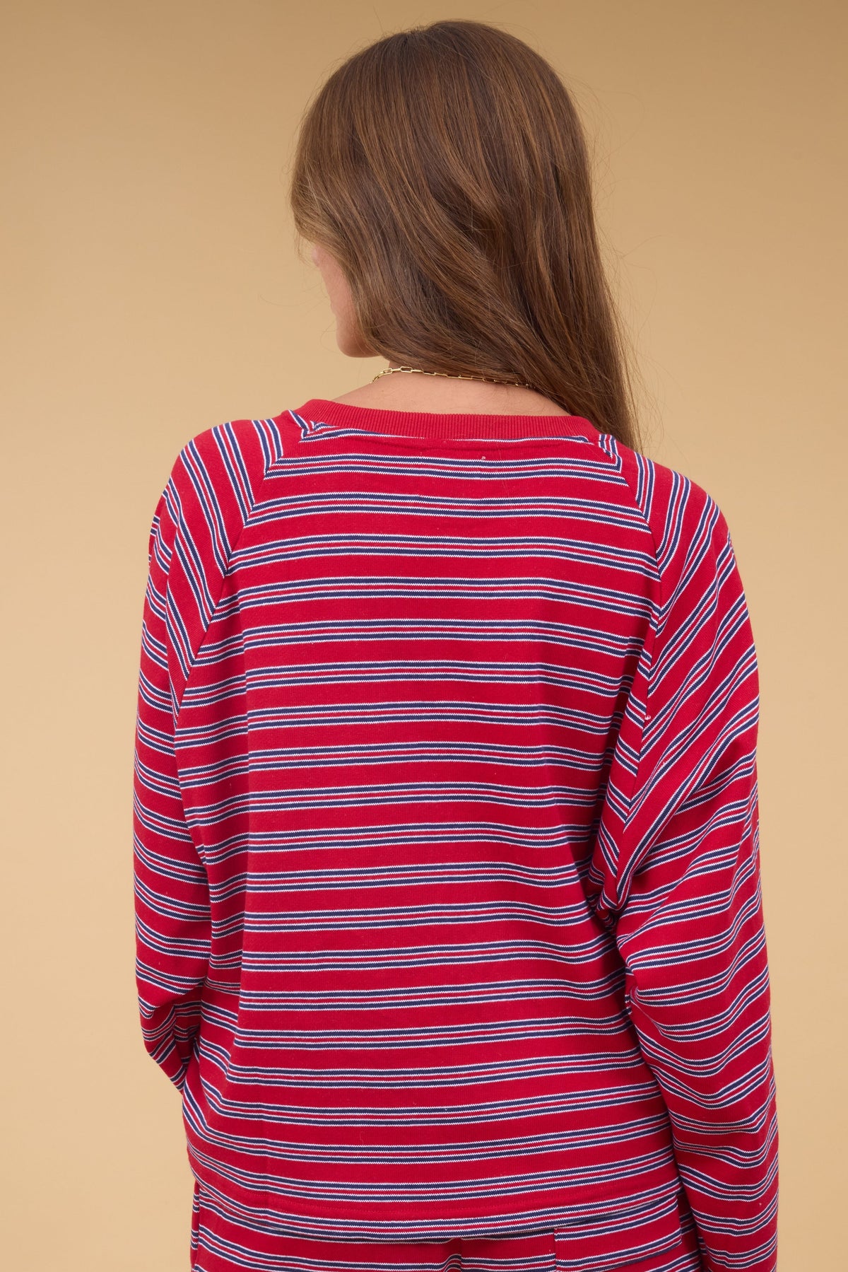 Back view of a woman wearing a red & navy stripe long sleeve sweatshirt.