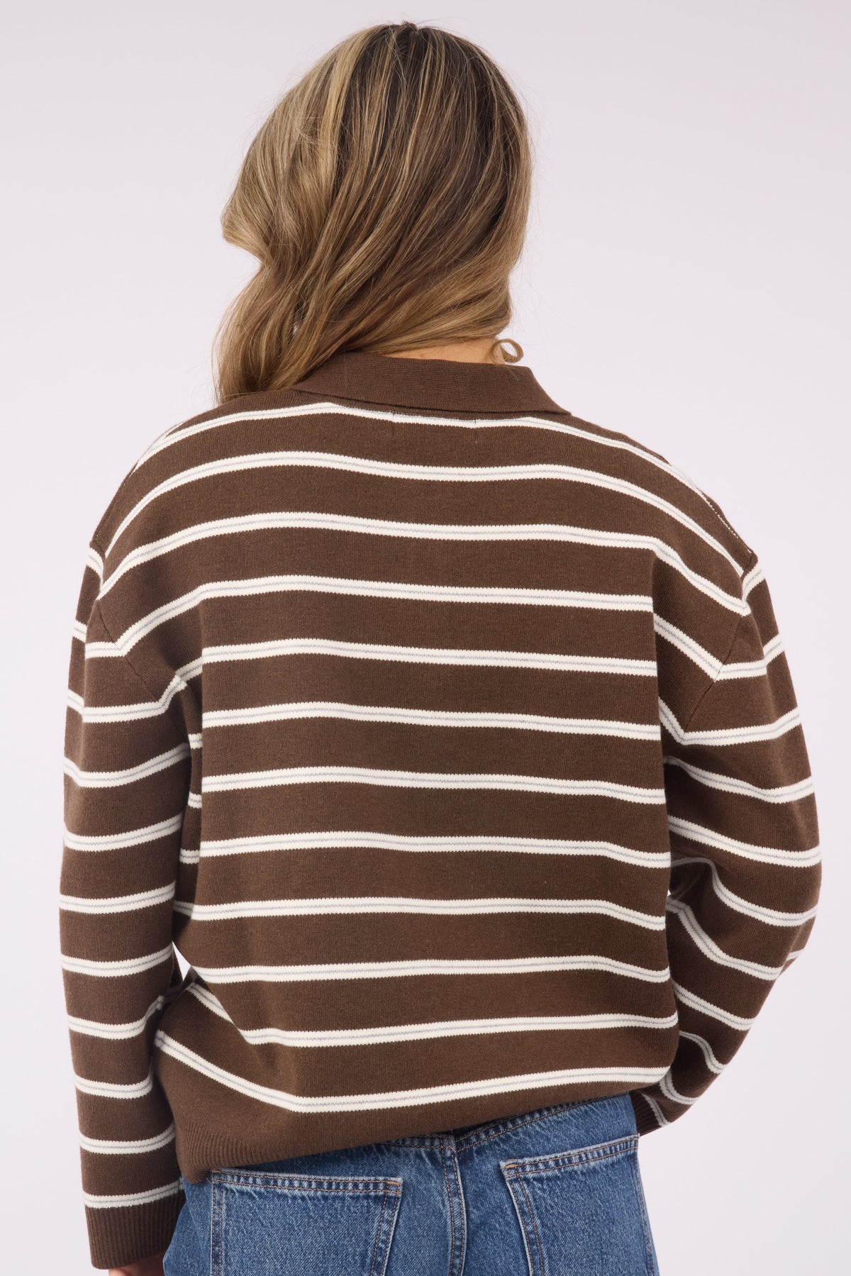 A back view of a woman wearing a brown & cream stripe pulloer sweater with long sleeves.