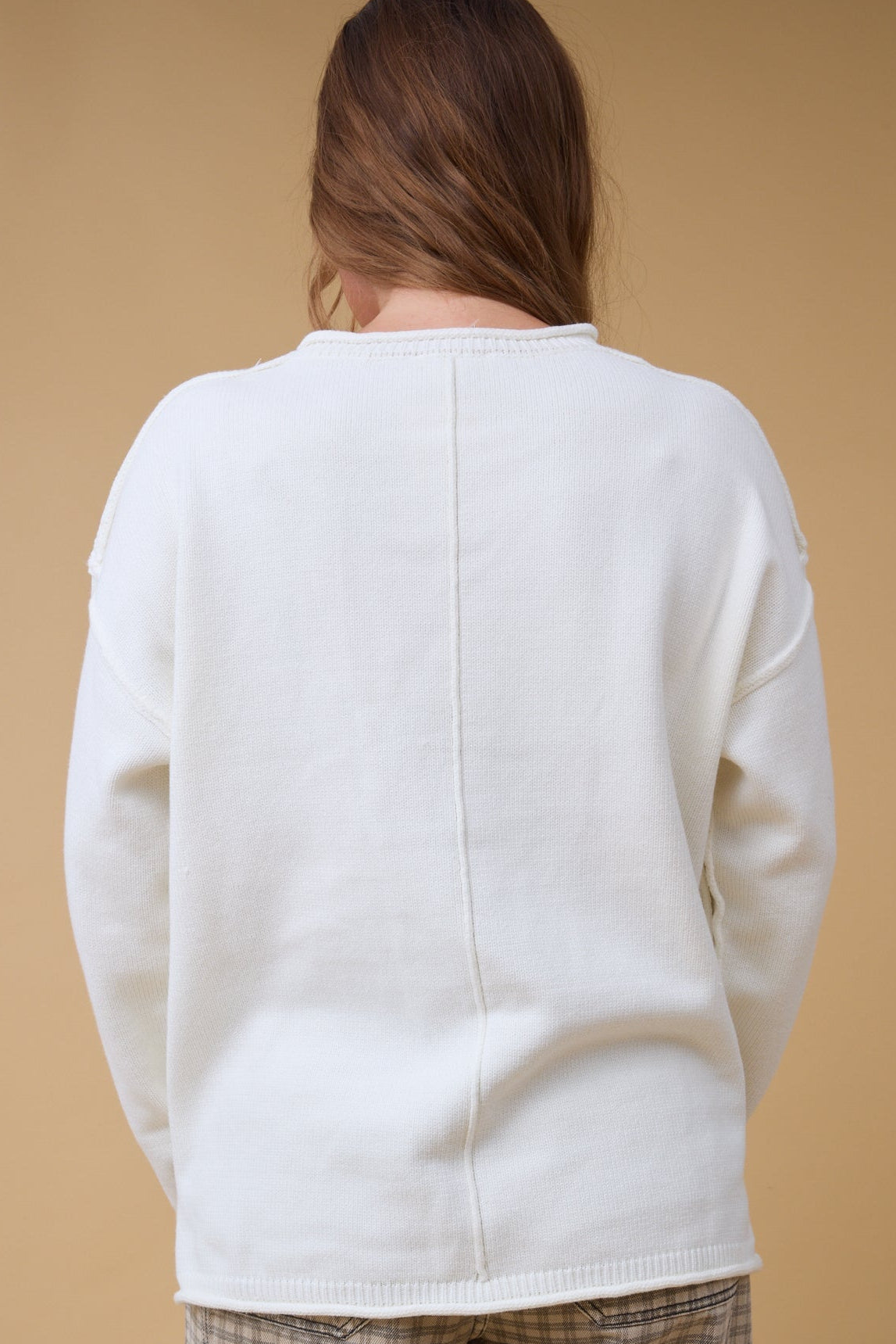 Back view of a woman wearing a cream pullover sweater with exposed seams and a decoaribe back center seam.