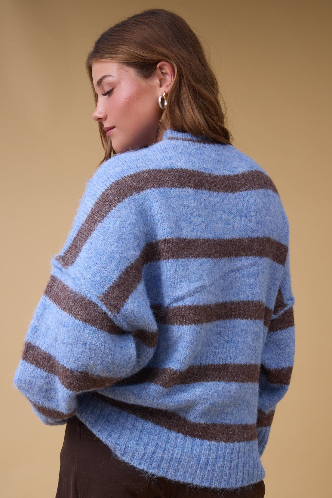 Back view of a young woman wearing a loose fitting pullover sweater in blue a& brown with drops shoulders.