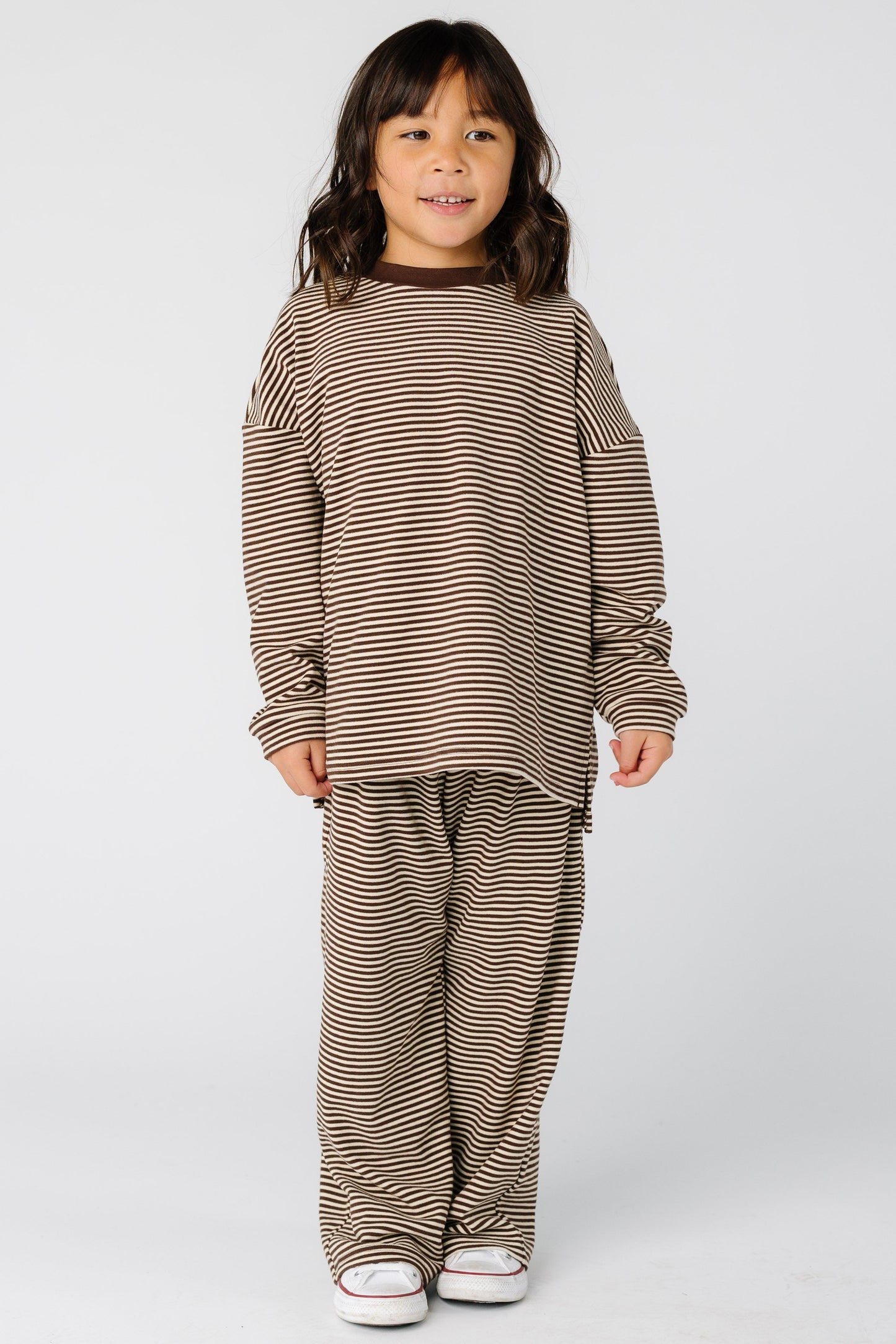 Girl wearing a loose fitting lounge set with long sleeves and full length pants in brown stripe