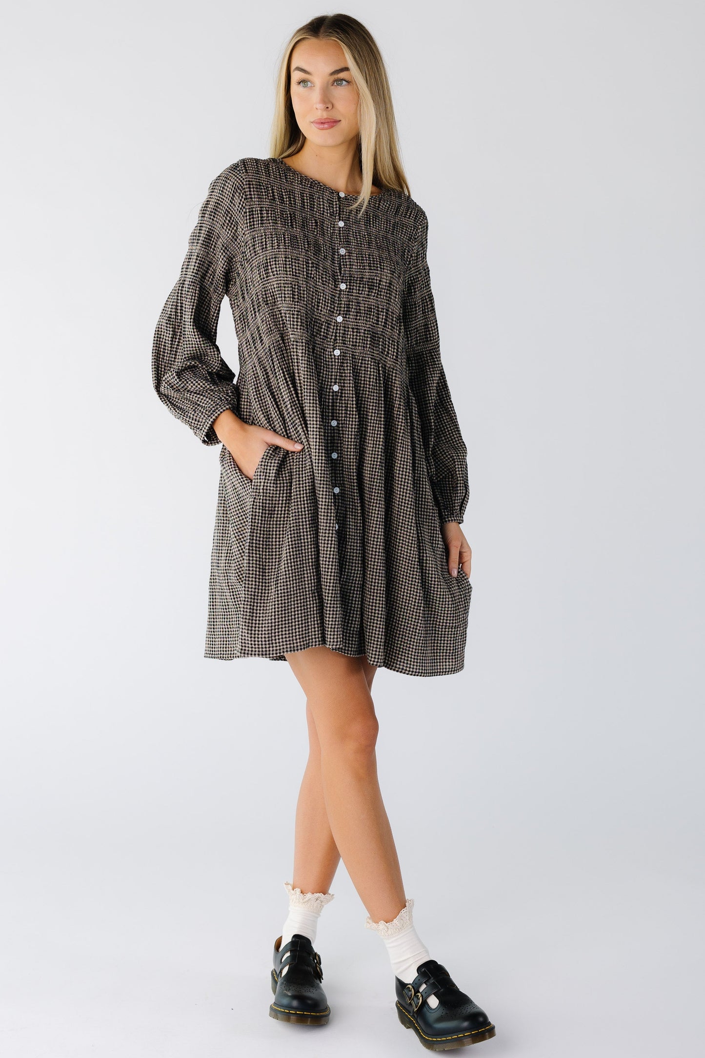 Woman wearing a black and tan knee length button down dress in black gingham with long sleeves and pockets