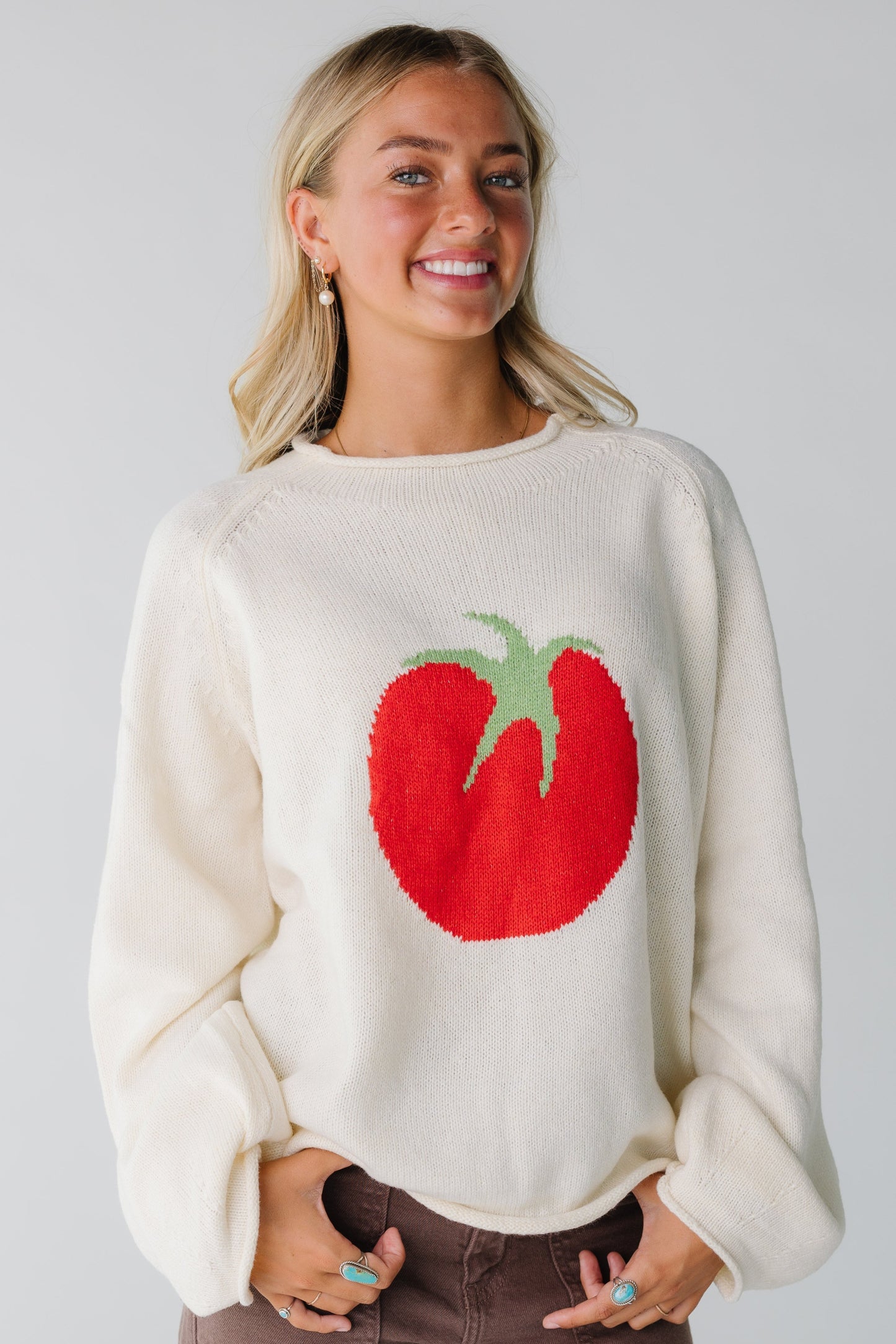 Woman wearing ivory oversized sweater with large red tomato graphic