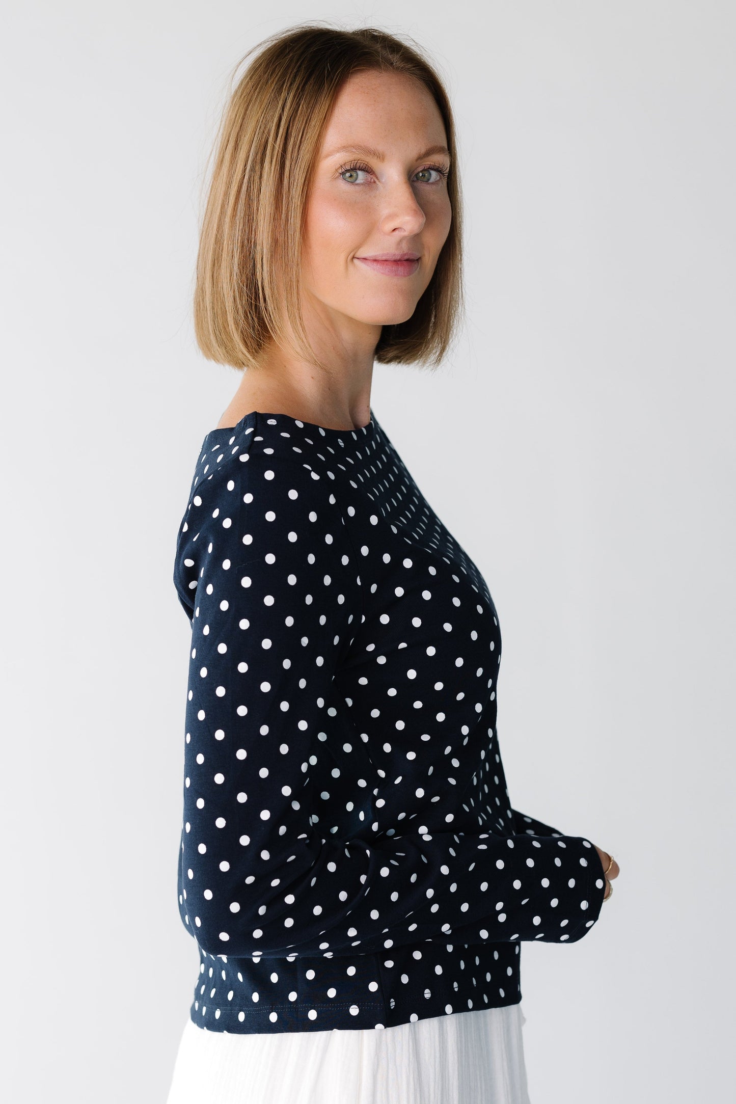 Side view of a woman wearing a modest navy polka dot top with long sleeves
