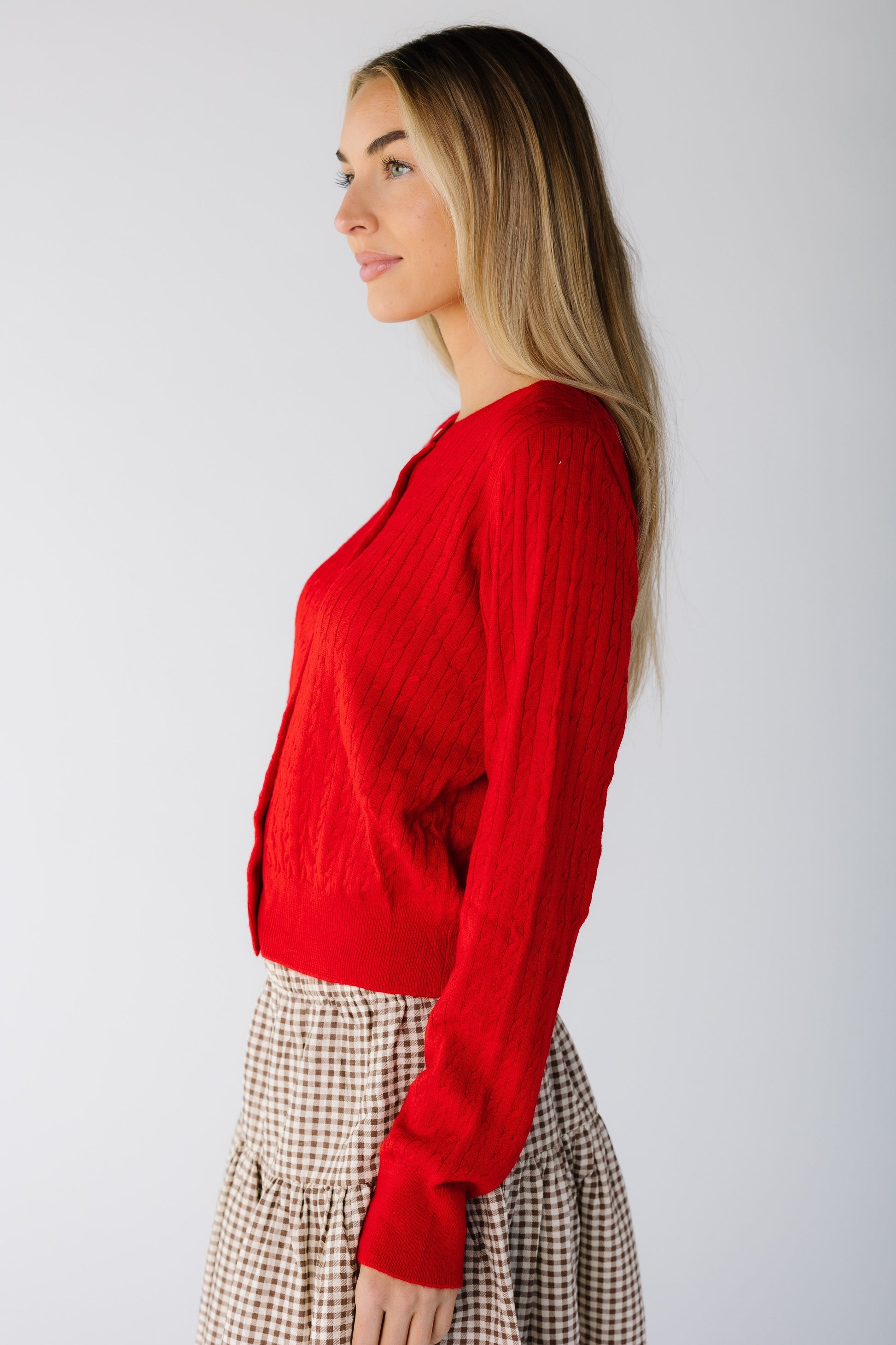 Side view of a woman wearing a long sleeve cable knit cardigan in red