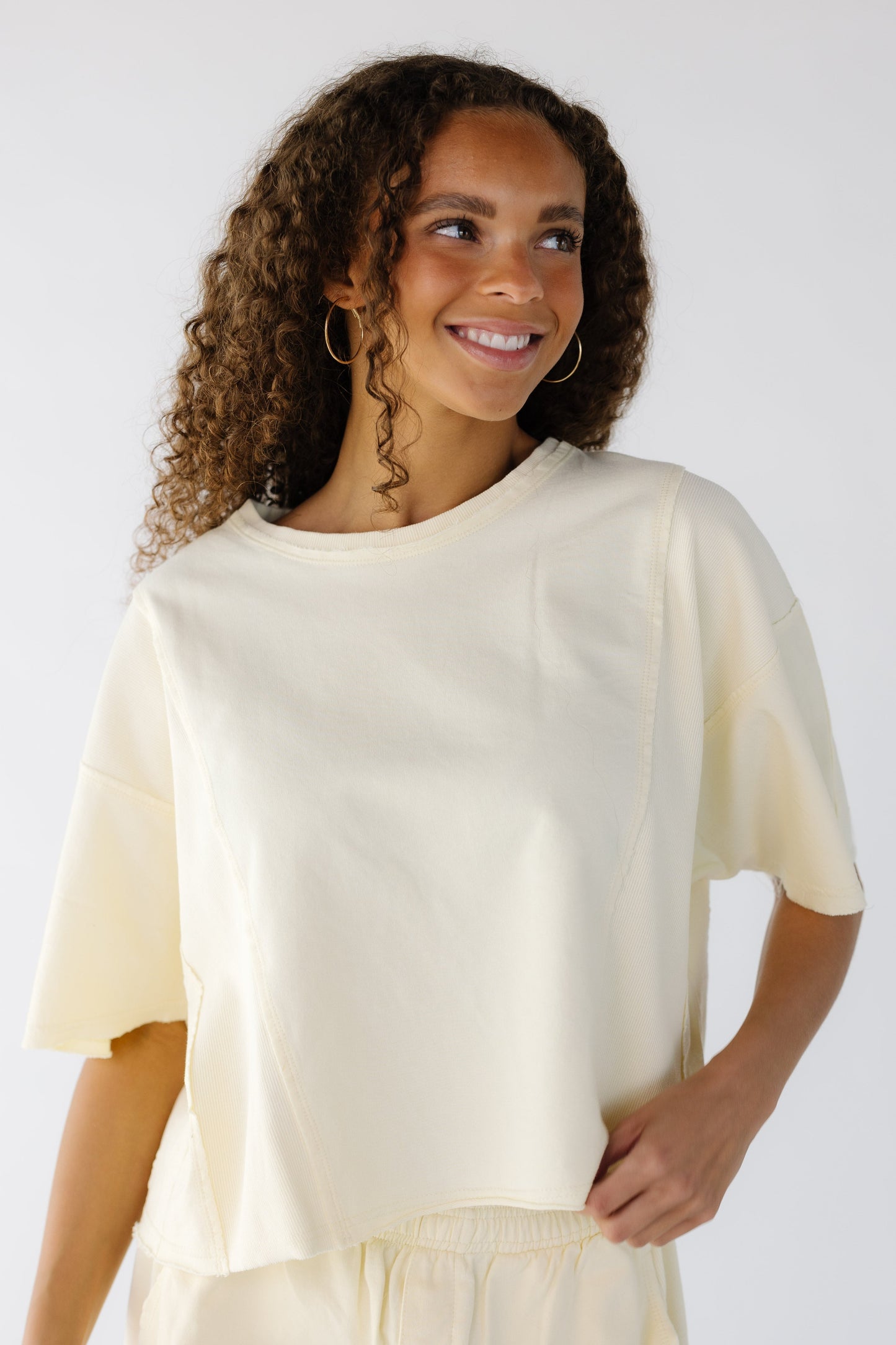 Teenage girl wearing a loose fitting yellow tee with rolled hems and elbow length sleeves.