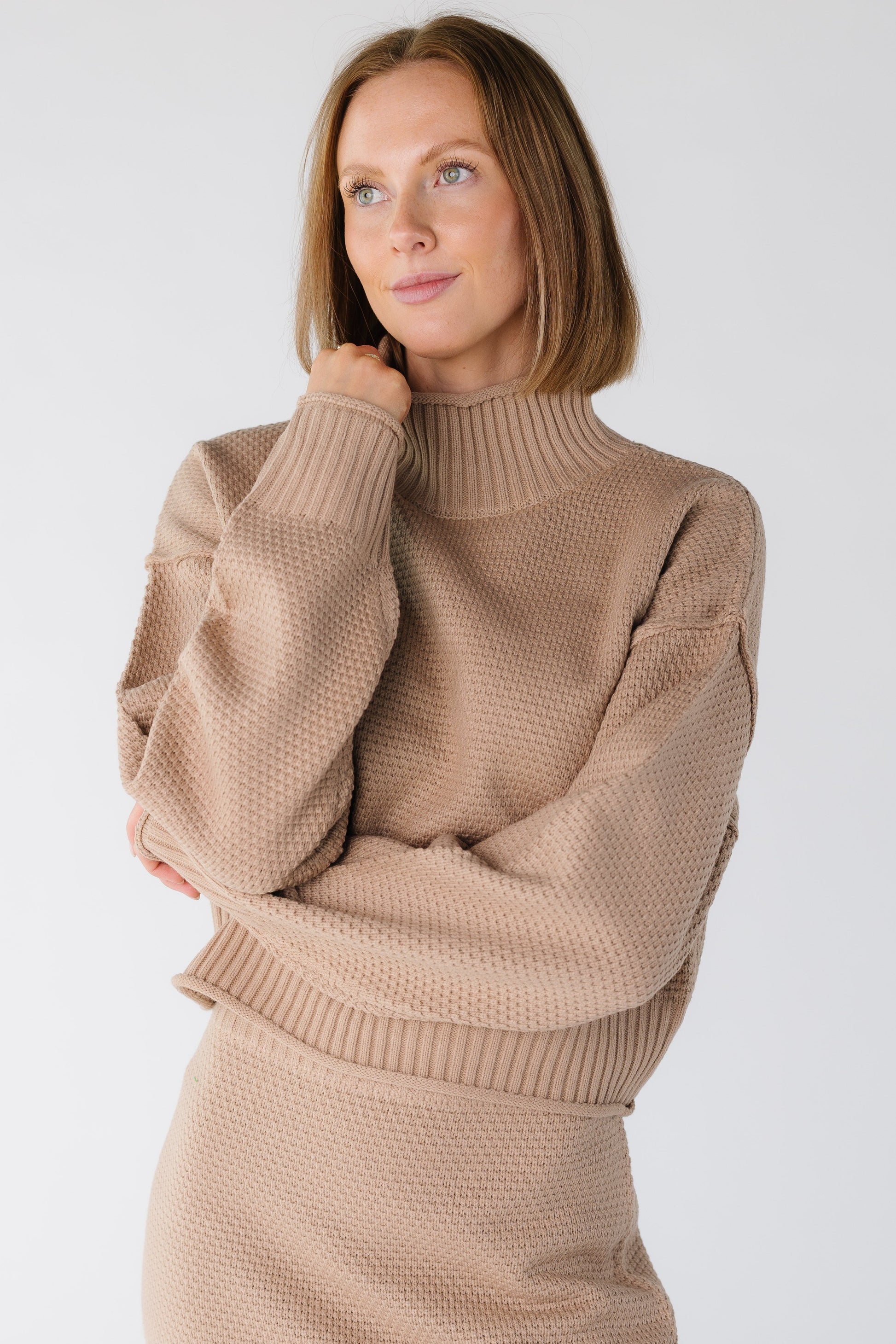 Close view of a woman wearing a long sleeve textured sweater with a ribbed turtleneck