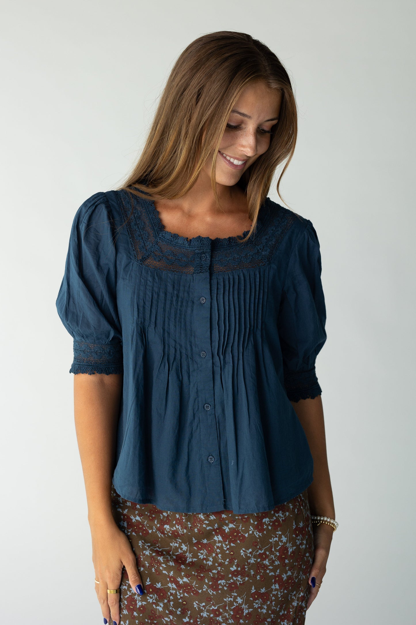 Woman wearing a navy button down blouse with lace square neckline and short sleeves