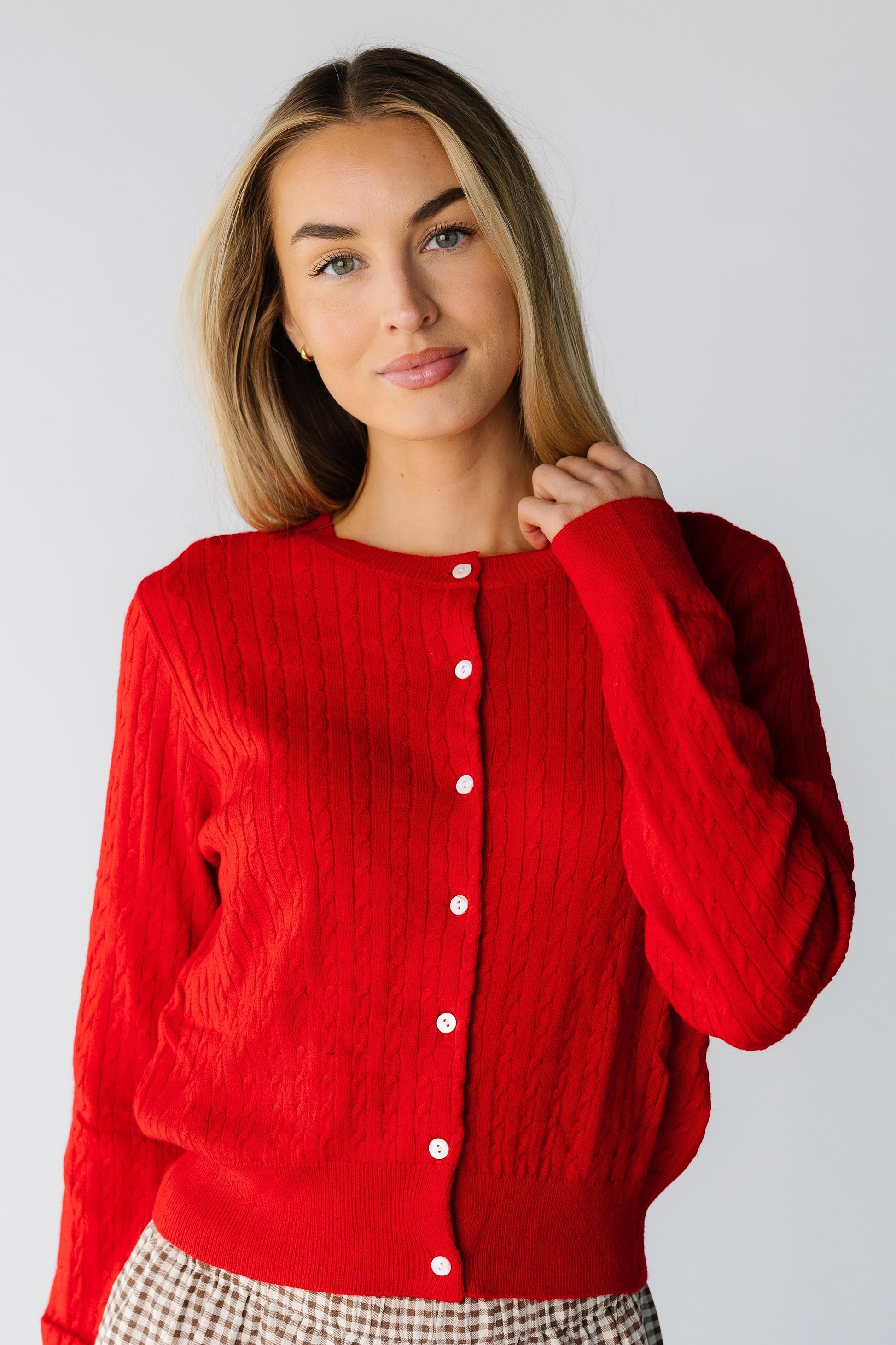 Woman wearing a red long sleeve cable knit cardigan with a round neckline and white buttons