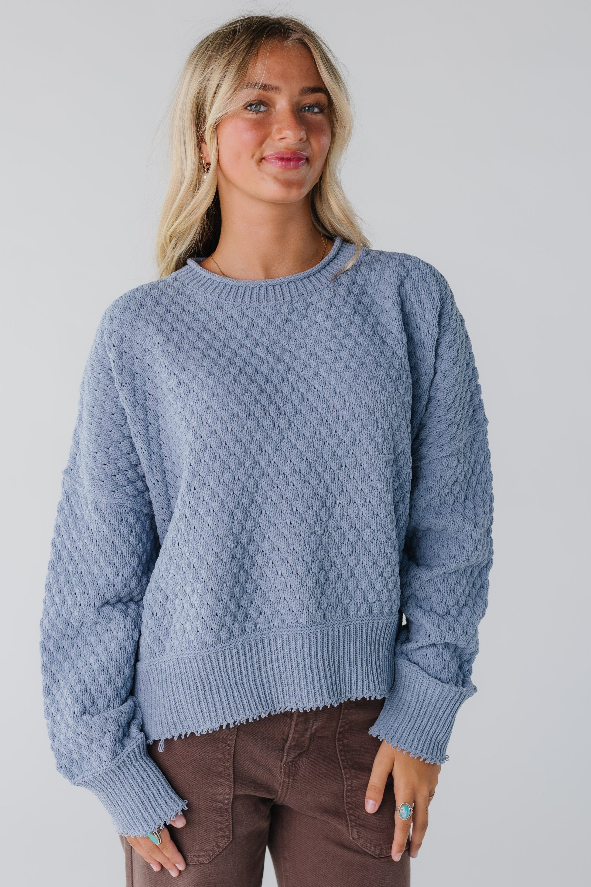 Woman wearing a blue textured sweater with long sleeves a a wide ribbed waist