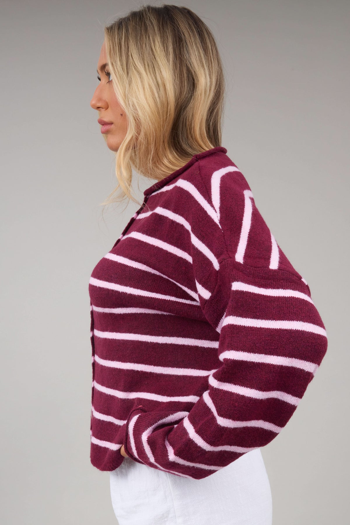 Side view of a young woman wearing a burgundy & pink stripe cardigan.