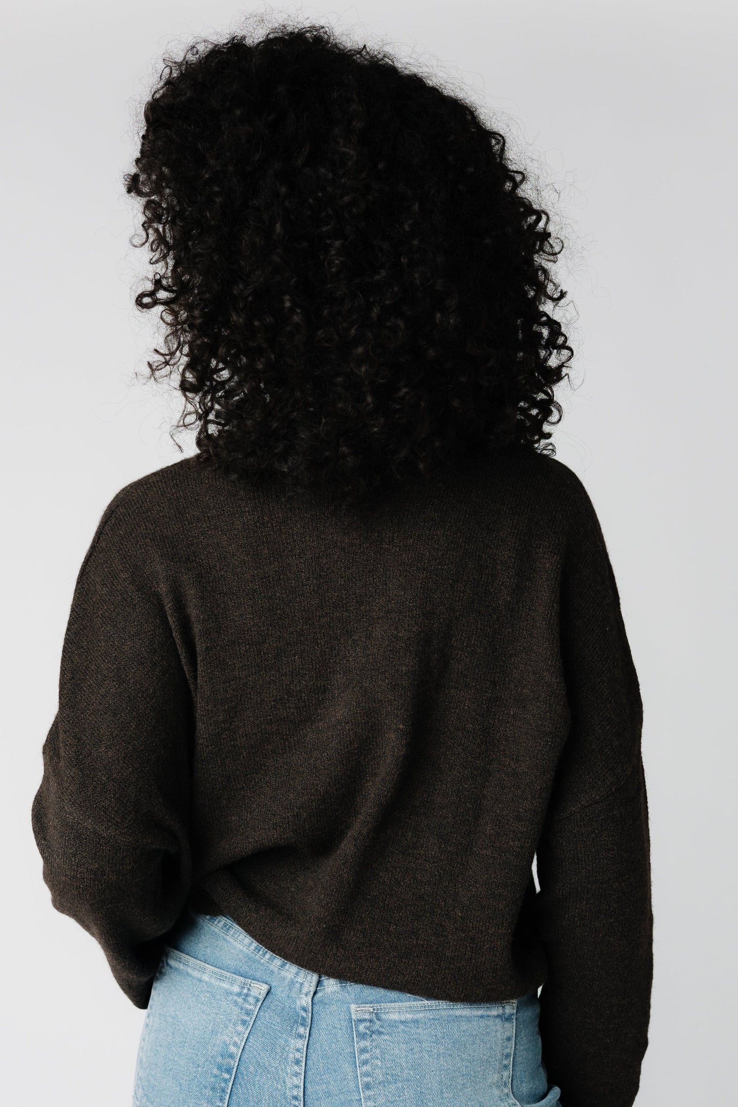 A back view of a woman wearing a brown sweater with long sleeves